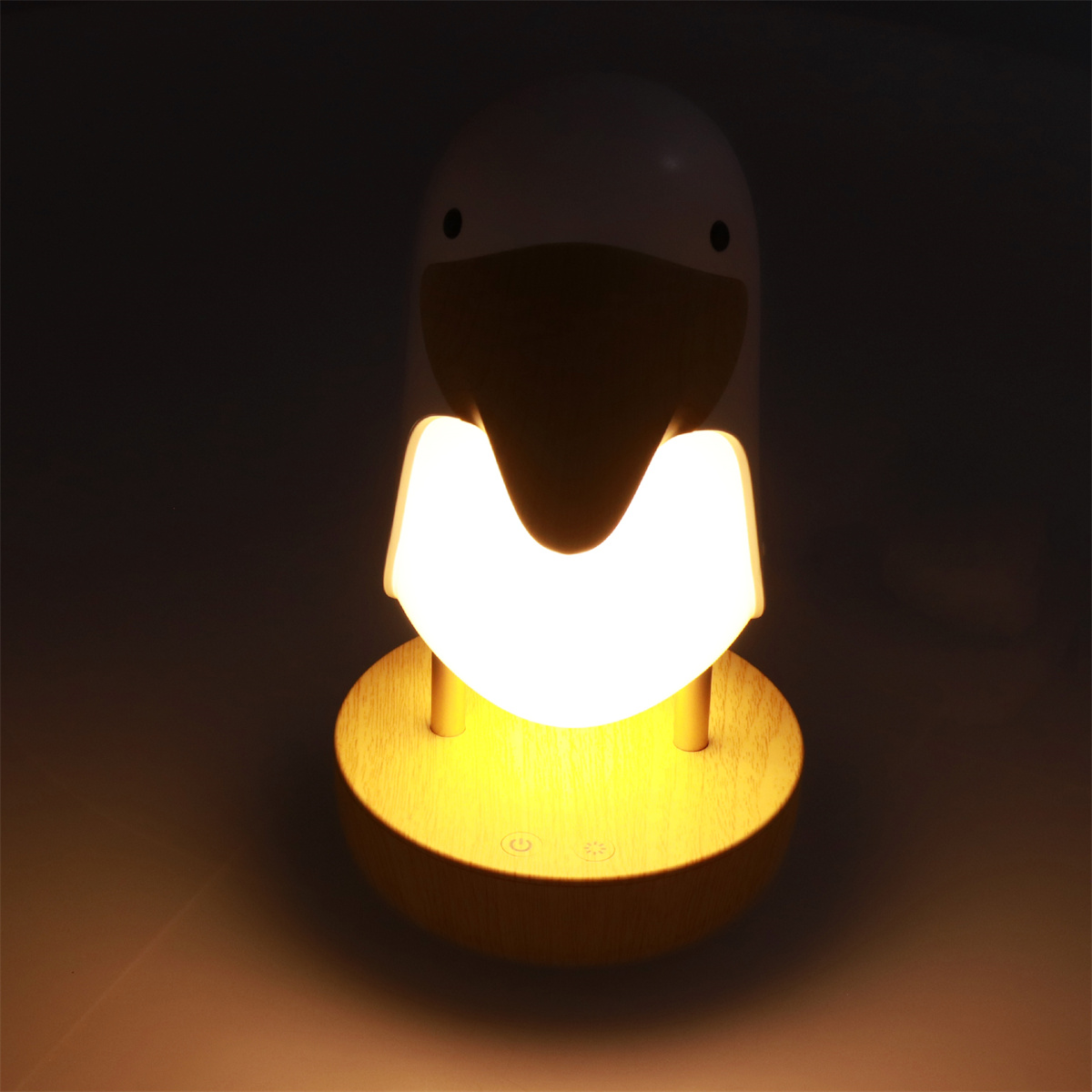 Ein Nachtlicht in Form eines Vogels. Es ist weiß mit einem Holzsockel und leuchtet.