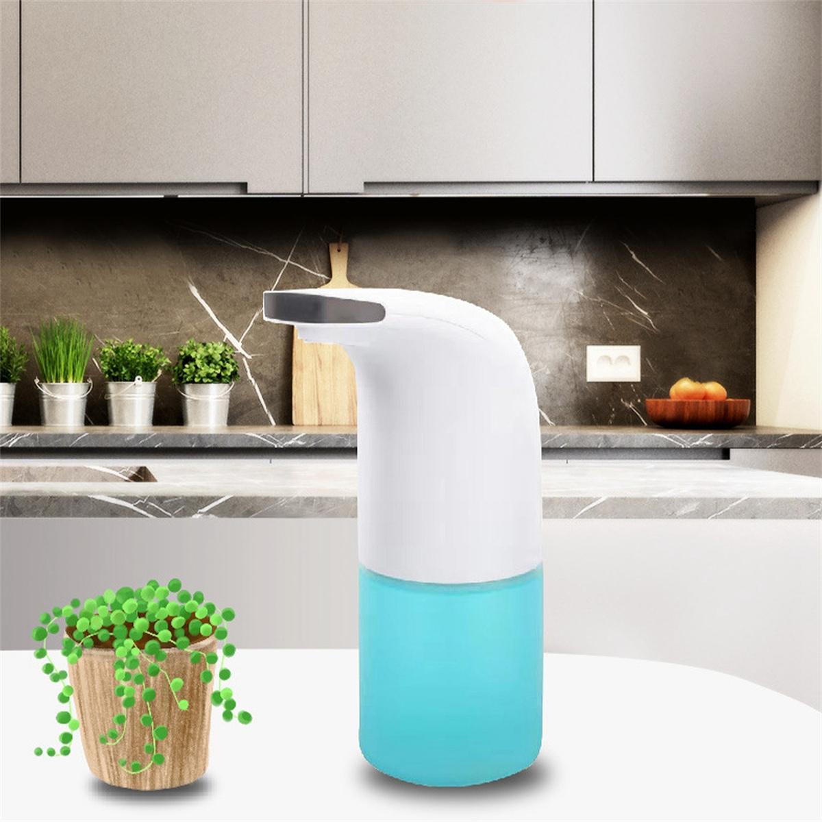 Weiß-blauer automatischer Seifenspender mit einer kleinen Pflanze in einem Topf auf einer Küchentheke.