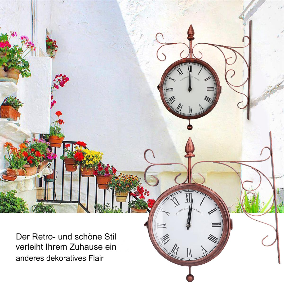 Zwei Bronzeuhren im Freien. Weißes Zifferblatt, römische Ziffern, um 12 Uhr. Dekorative Halterungen. Weißer Gebäudehintergrund, Blumen.