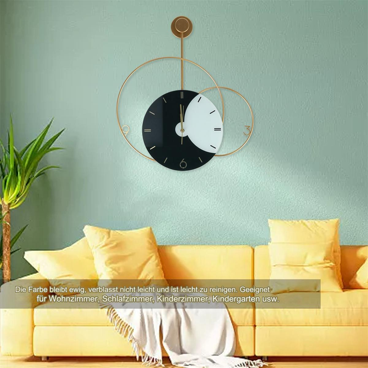 Eine goldene Metalluhr mit schwarz-weißem Zifferblatt an einer Wand. Gelbe Kissen und Couch im Bild.