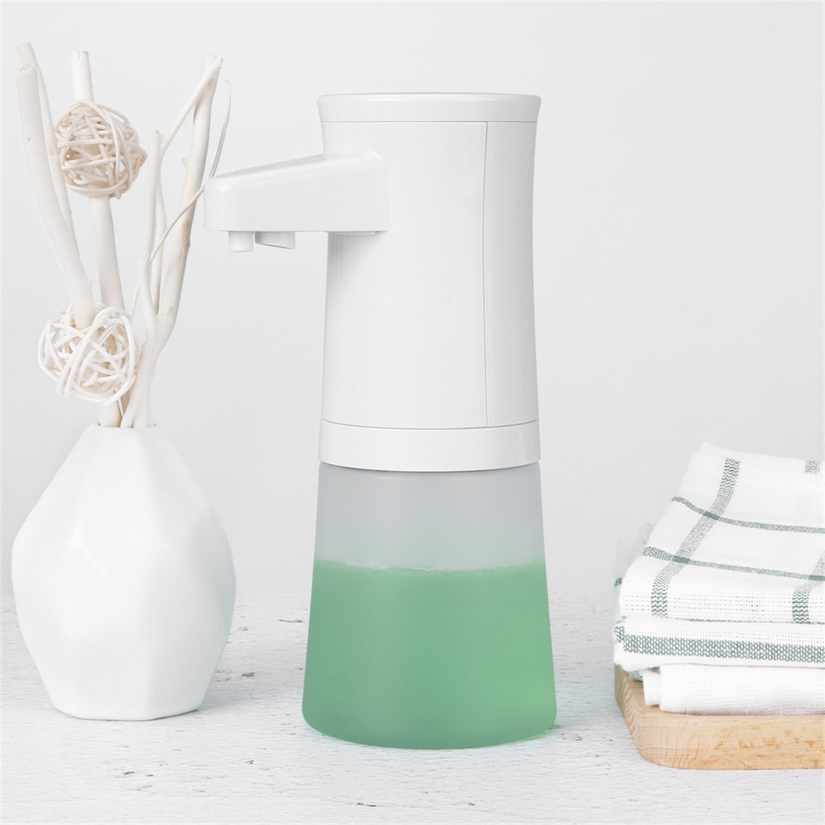 Weißer Seifenspender mit grüner Seife, weißer Vase und Handtuch. Weißer Hintergrund.
