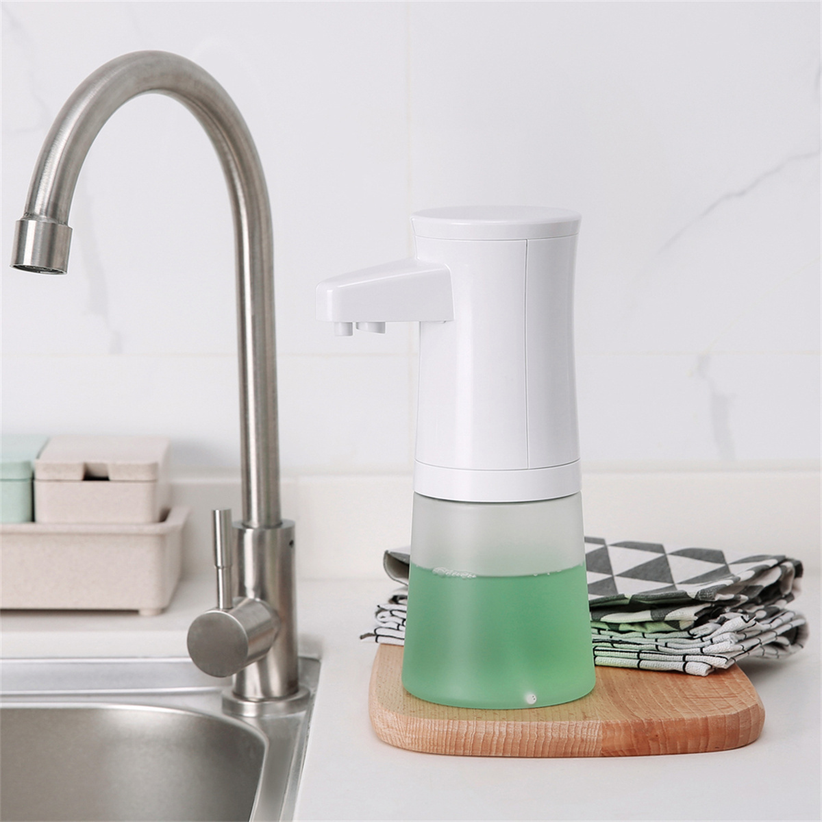 Weißer automatischer Seifenspender mit grüner Seife, silberner Wasserhahn, Holzbrett und Handtuch.