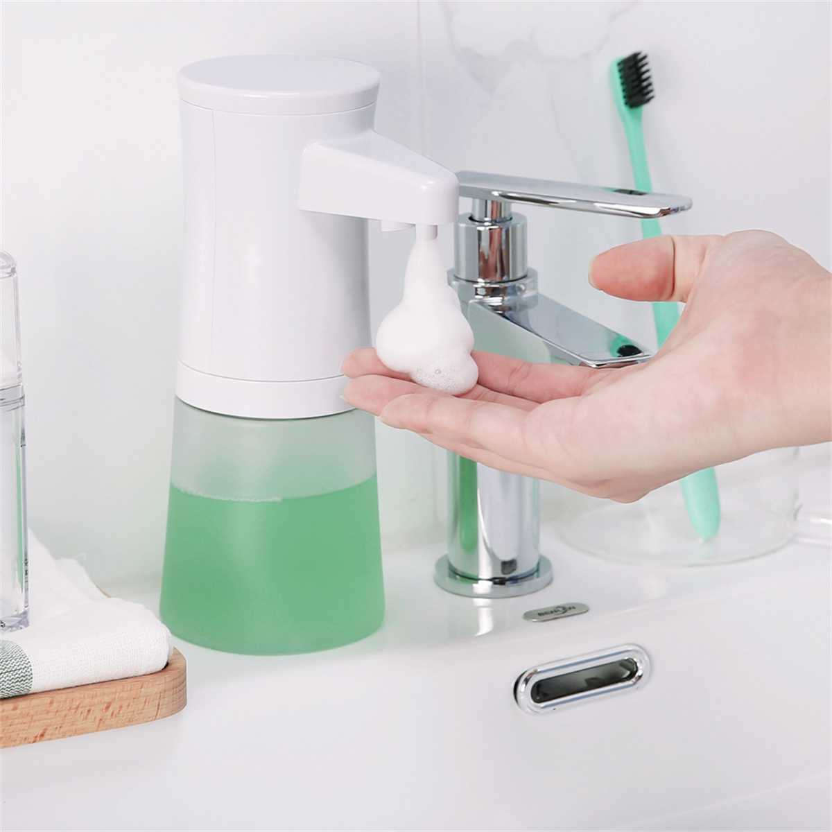 Ein weißer, automatischer Seifenspender gibt Schaum in eine Hand ab. Im Hintergrund befinden sich ein Waschbecken, ein Wasserhahn und eine Zahnbürste.