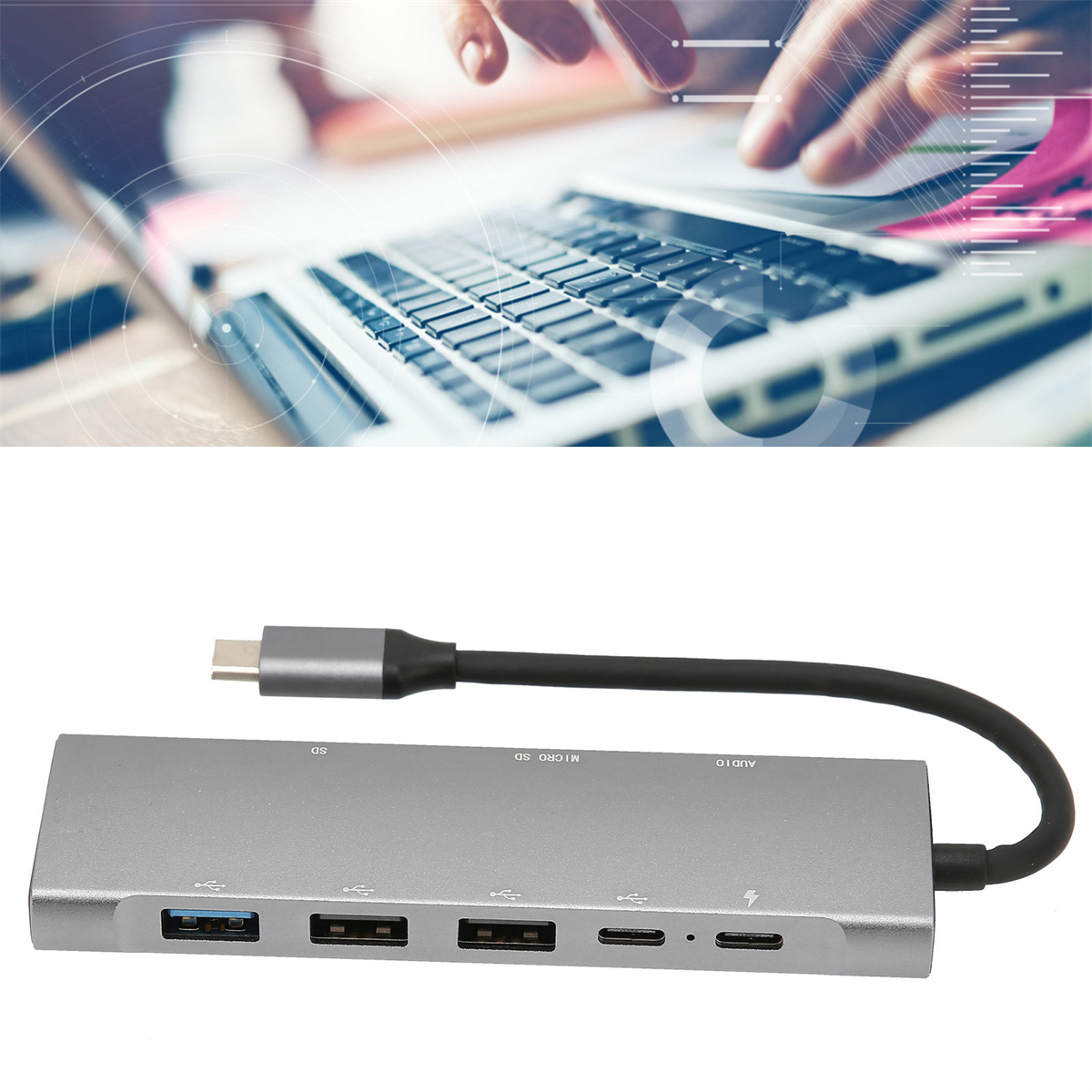 Ein silberner Multiport-Adapter mit Anschlüssen und einem Kabel. Im Hintergrund befindet sich ein Laptop mit Grafiken auf dem Bildschirm.