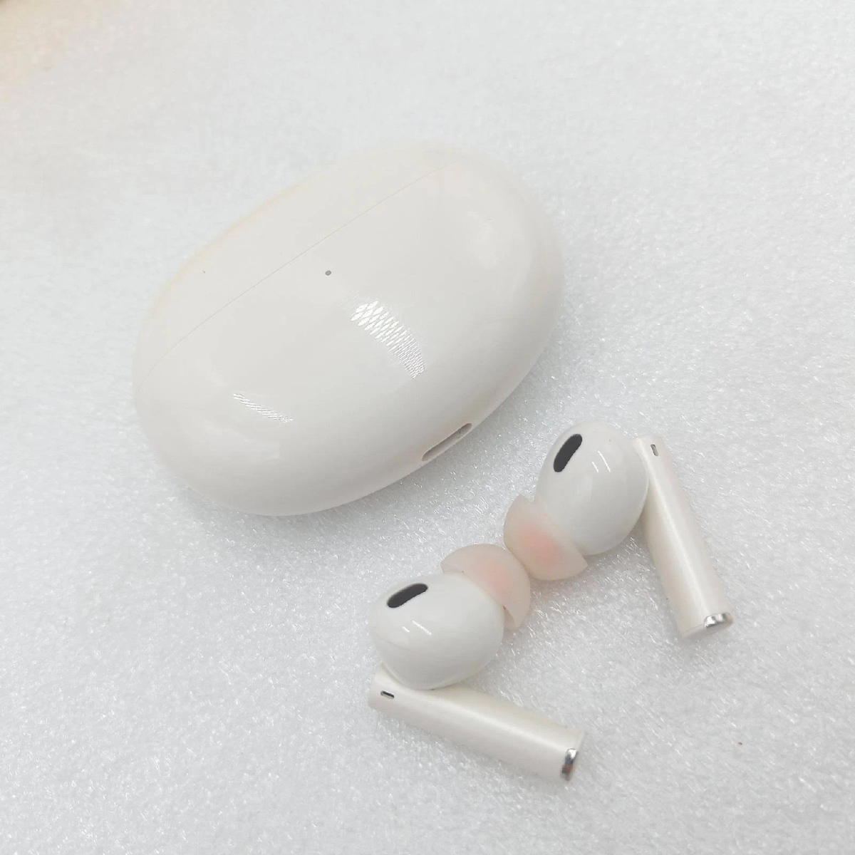 Auricolari bianchi con custodia di ricarica, su una superficie bianca. Gli auricolari sono parzialmente fuori dalla custodia.