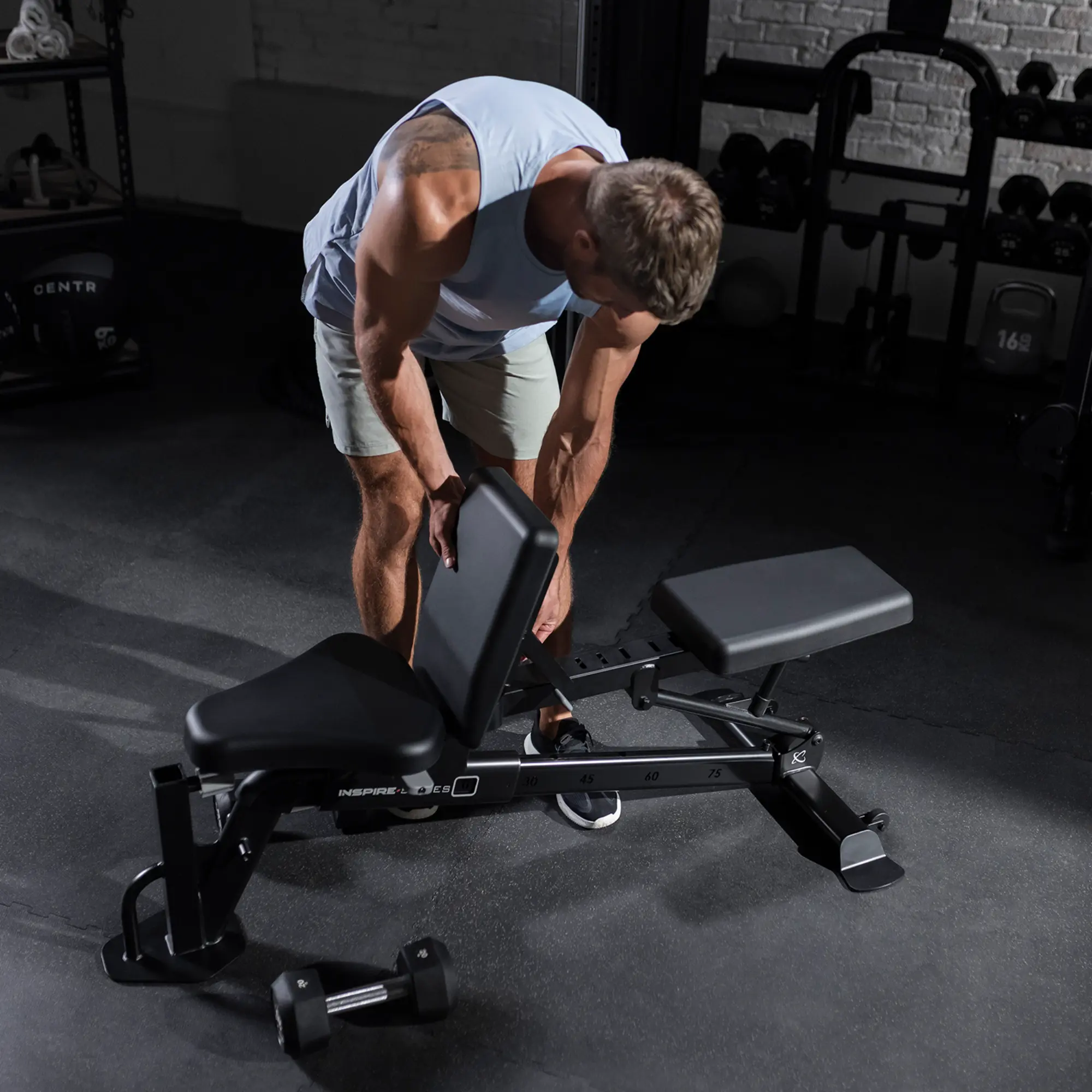 Man adjusting a black weight bench in a gym. Dumbbell on the floor.