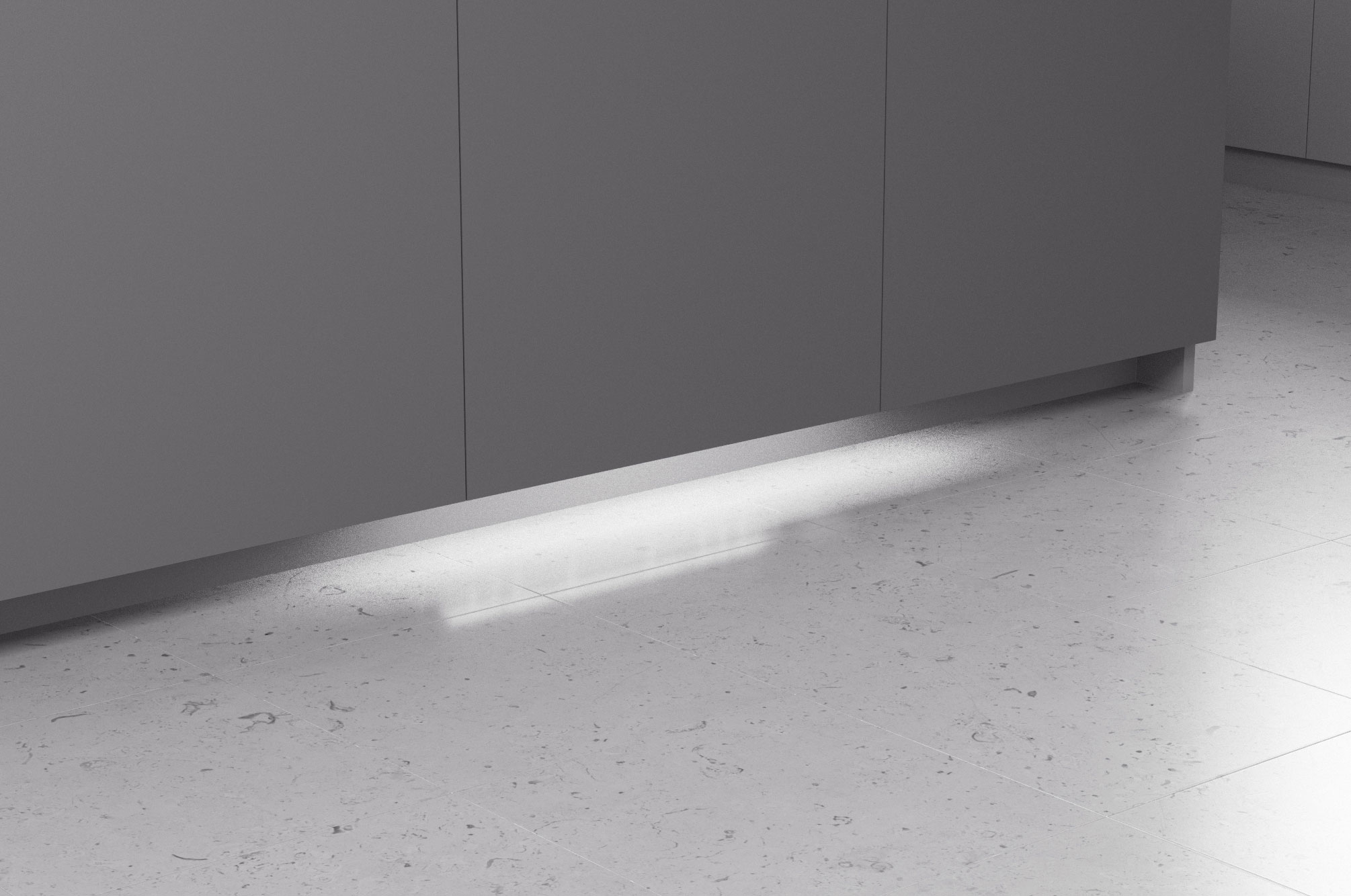 Nahaufnahme eines Lichtstreifens unter einem grauen Schrank auf hellem Steinboden.