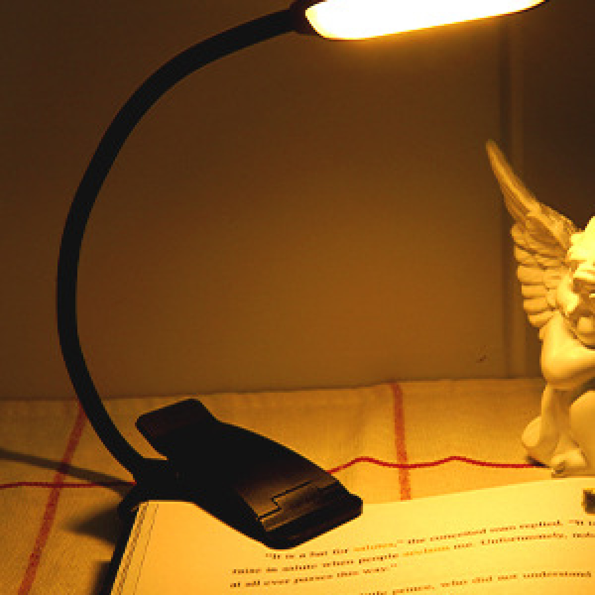 Czarna lampka do czytania LED z klipsem oświetlająca książkę, z małą statuetką w tle.