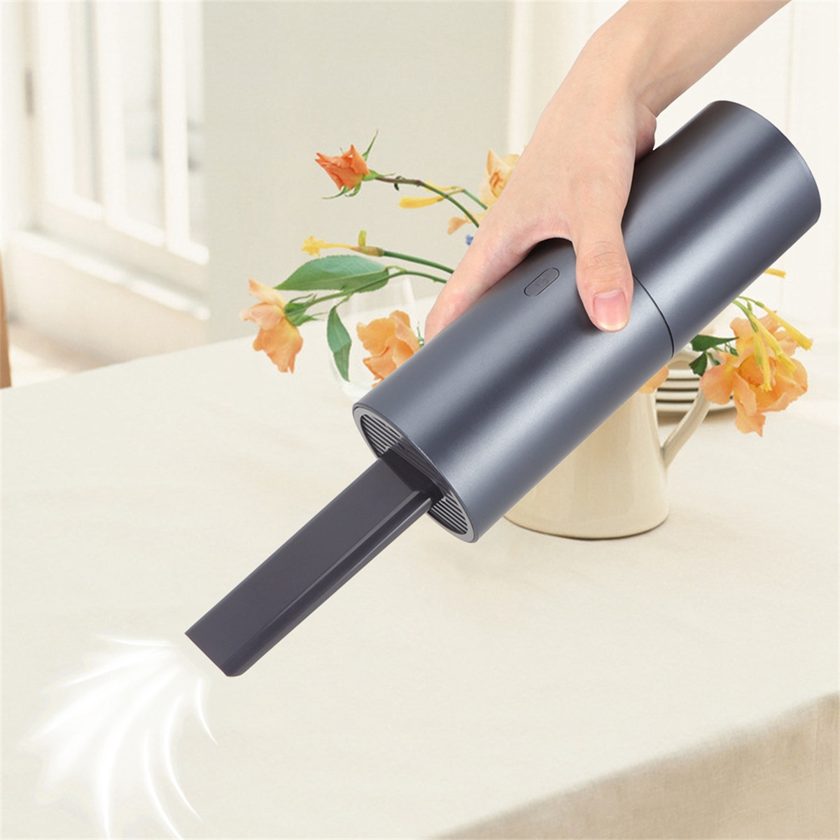 Eine Person hält einen dunkelgrauen Staubsauger über einem Tisch, mit einer Blumenvase.