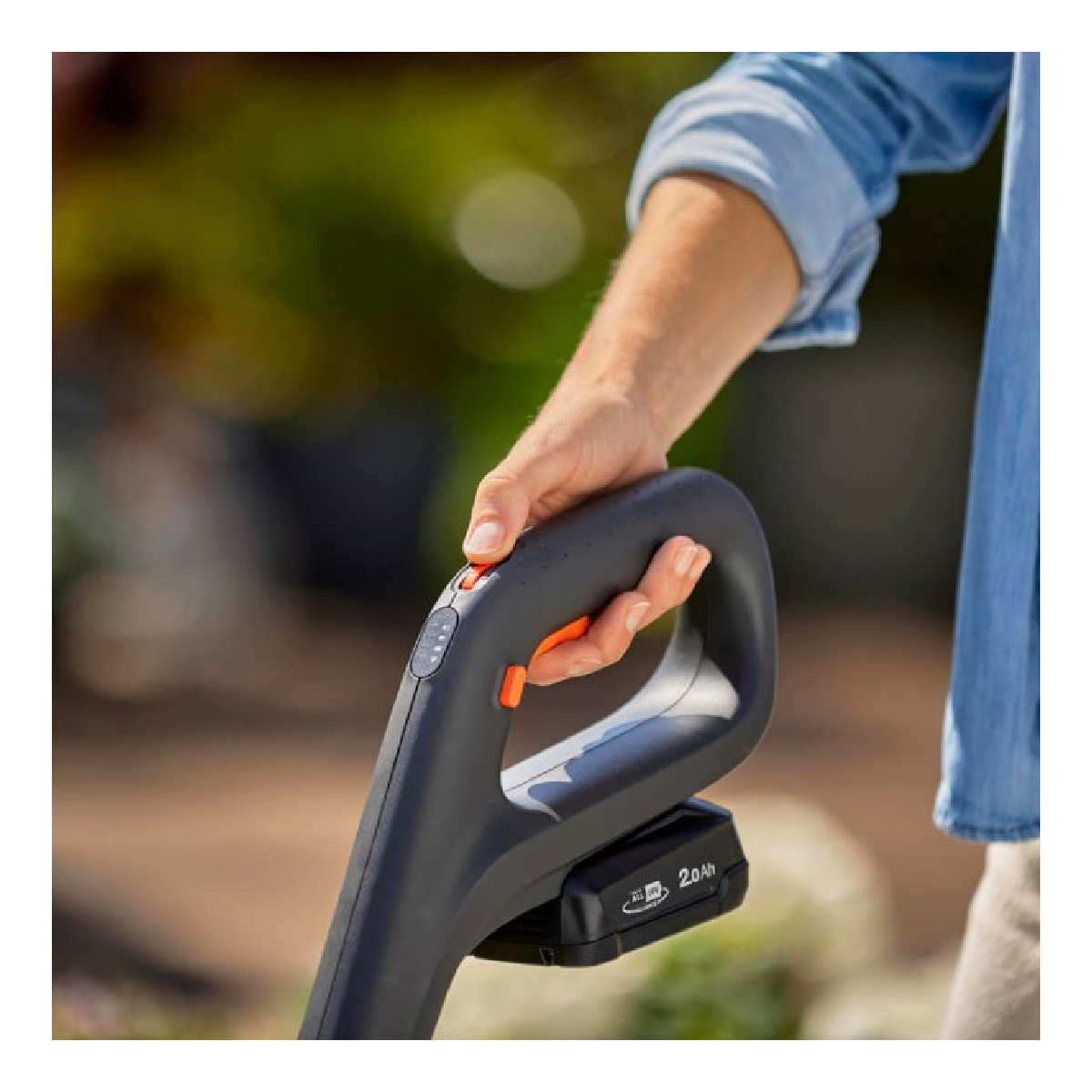 A hand holding a black tool with an orange button. The tool has a battery attached. Blue shirt.