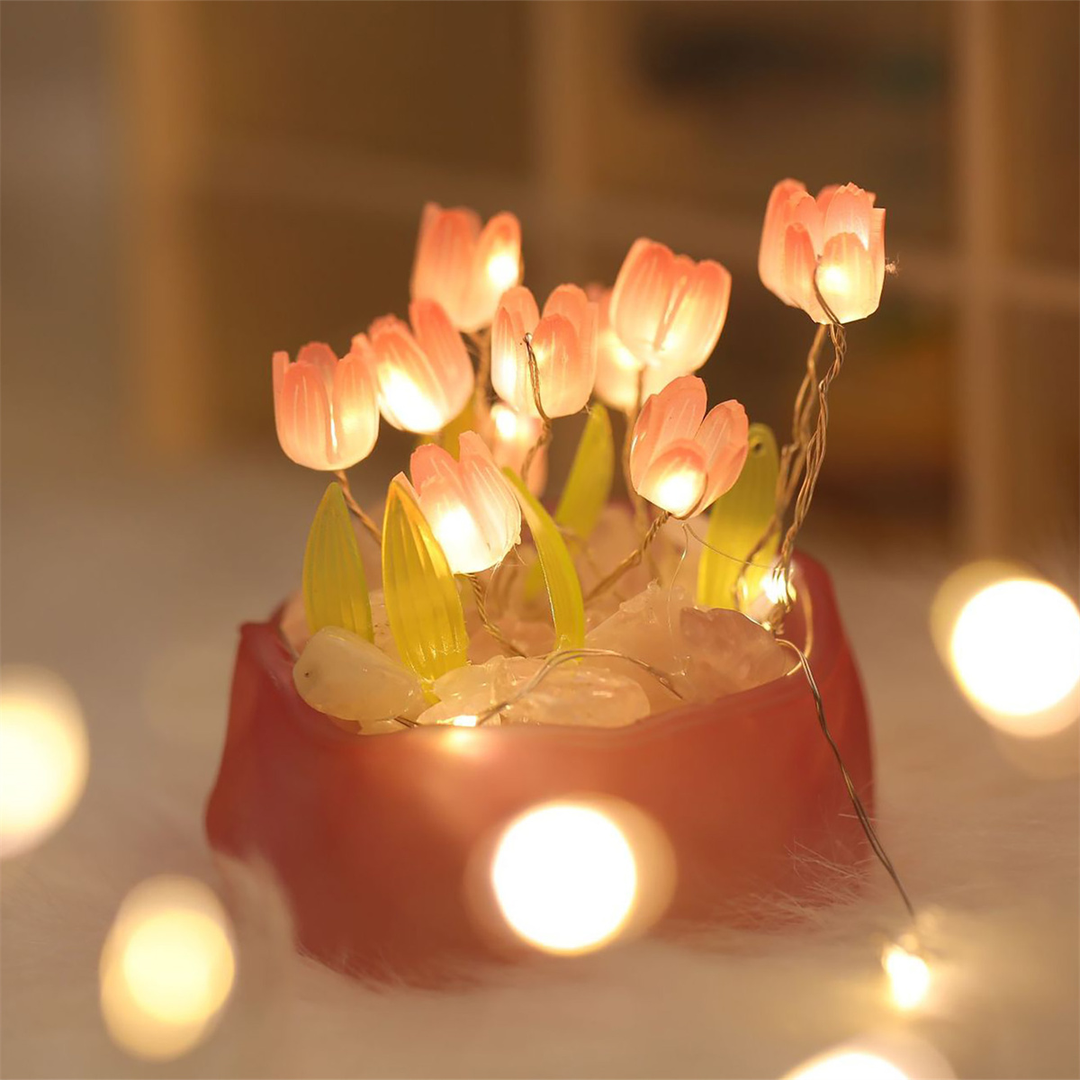 Eine kleine Anordnung von beleuchteten, rosafarbenen, tulpenförmigen Lichtern in einem roten Topf.