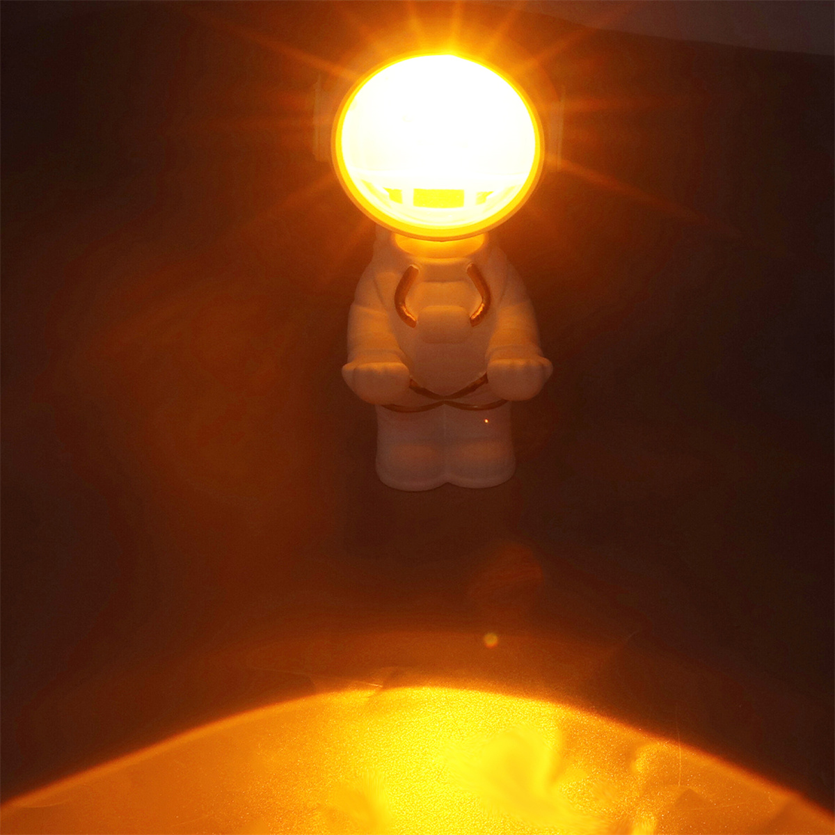Eine weiße astronautenförmige Lampe, die warmes, oranges Licht ausstrahlt. Dunkelbrauner Hintergrund.