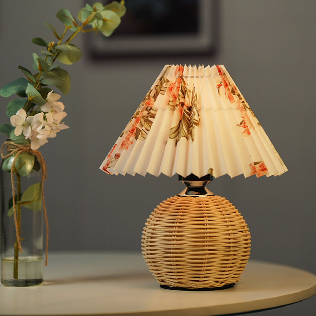 Eine kleine Tischlampe mit gewebtem Fuß und einem Lampenschirm mit floralem Muster auf einem Tisch.