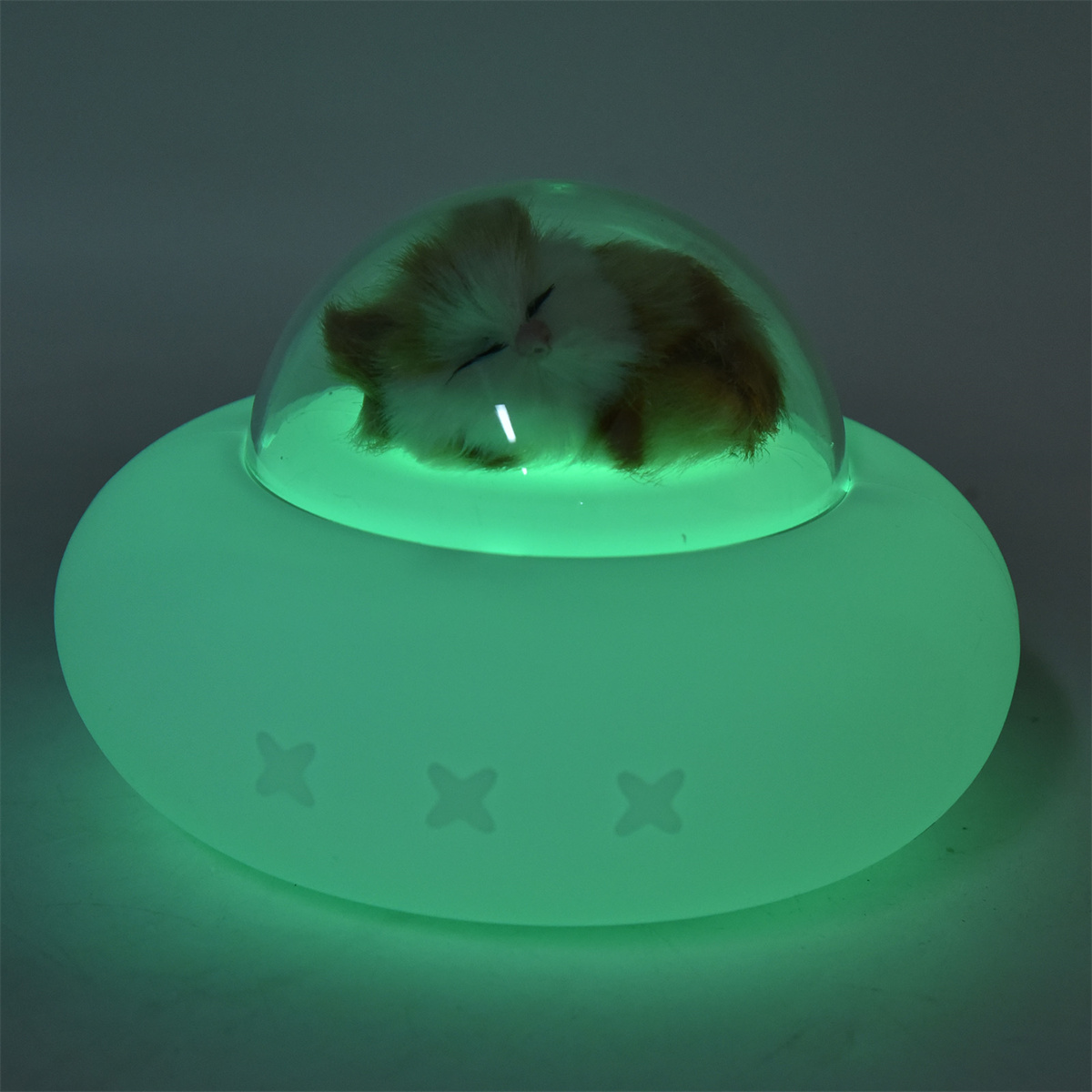 Grün leuchtende, außerirdisch geformte Lampe mit schlafender Katze in einer Kuppel.