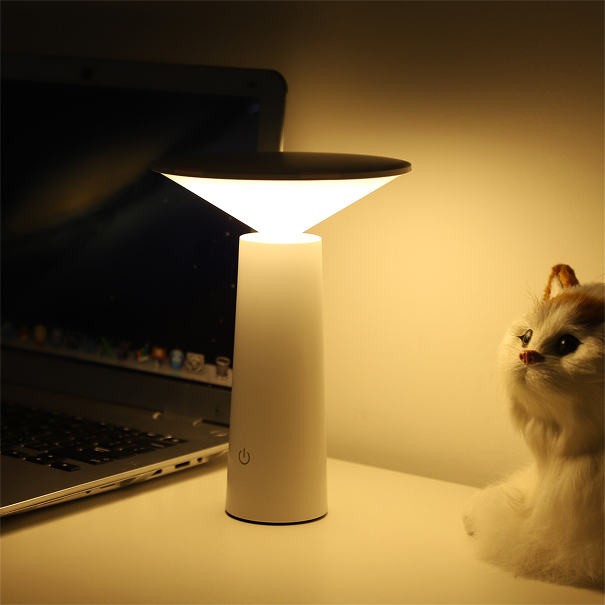 Weiße Tischlampe mit Laptop und Katzenfigur.