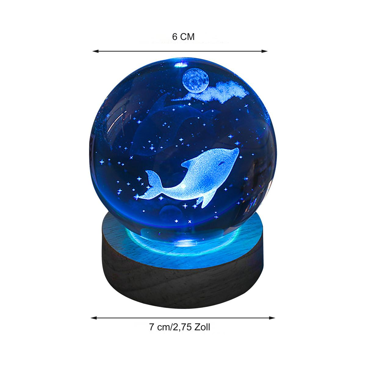 Glaskugel mit Delfin auf Holzsockel, beleuchtet von blauem Licht.