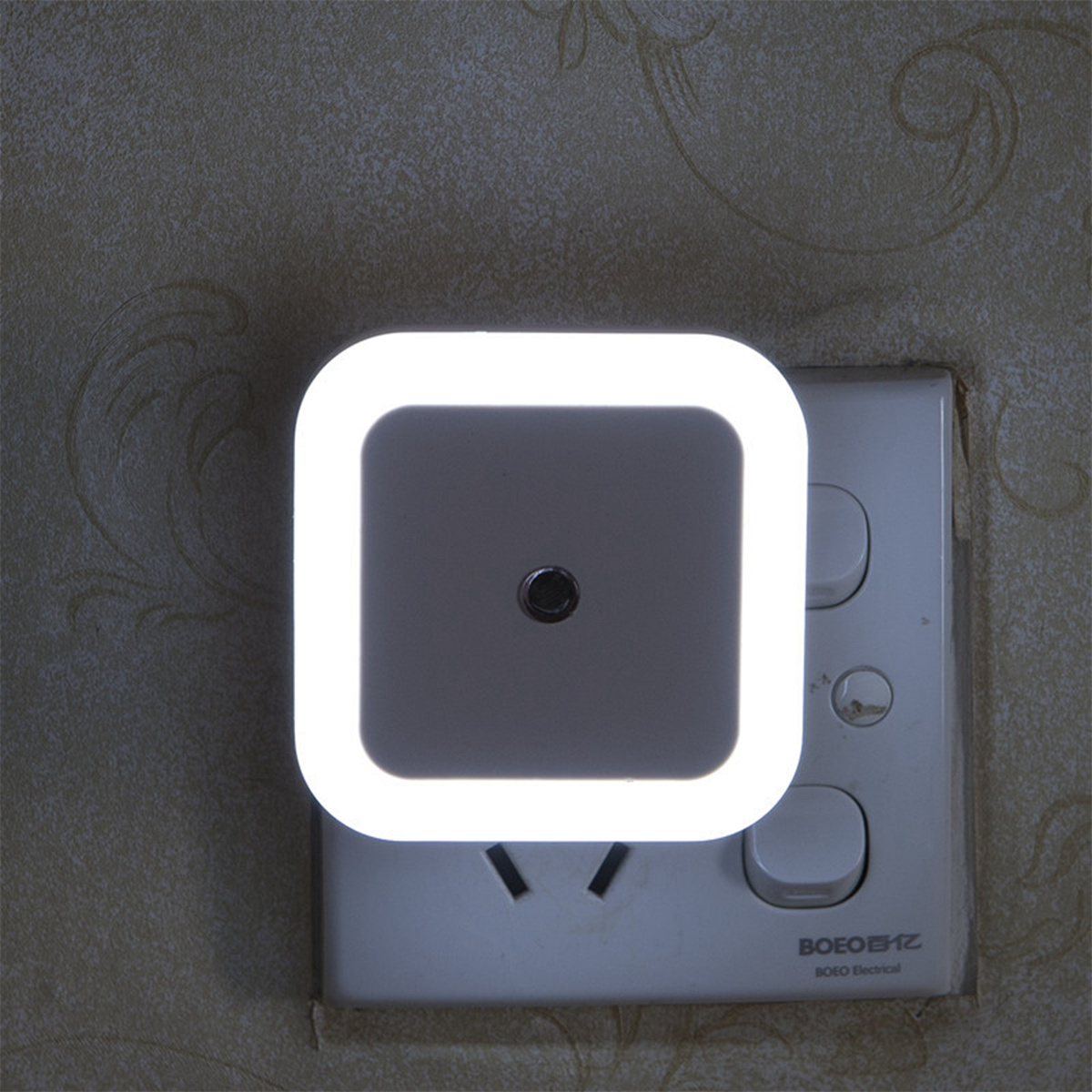Ein weißes Nachtlicht mit quadratischer Form und hellem weißen Licht. Es ist in eine Steckdose gesteckt.