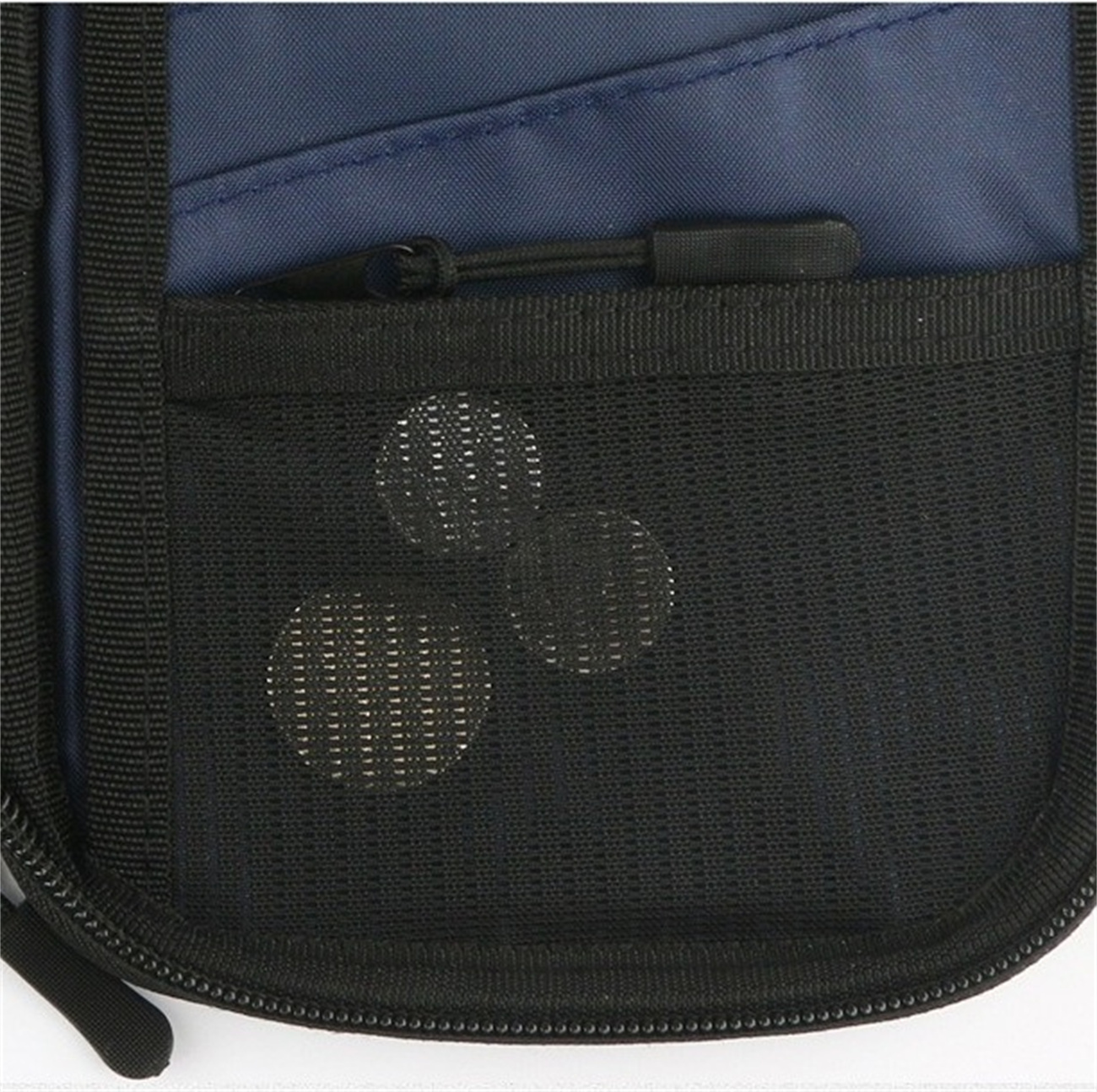 Nahaufnahme einer schwarzen Netztasche auf einer dunkelblauen Tasche. Drei kleine, runde, metallische Objekte sind sichtbar.