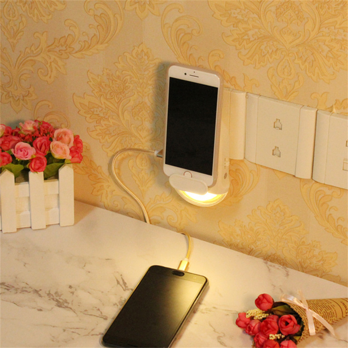 Ein Telefon, das in einer Steckdose geladen wird. Ein anderes Telefon liegt mit Blumen auf einem Tisch.