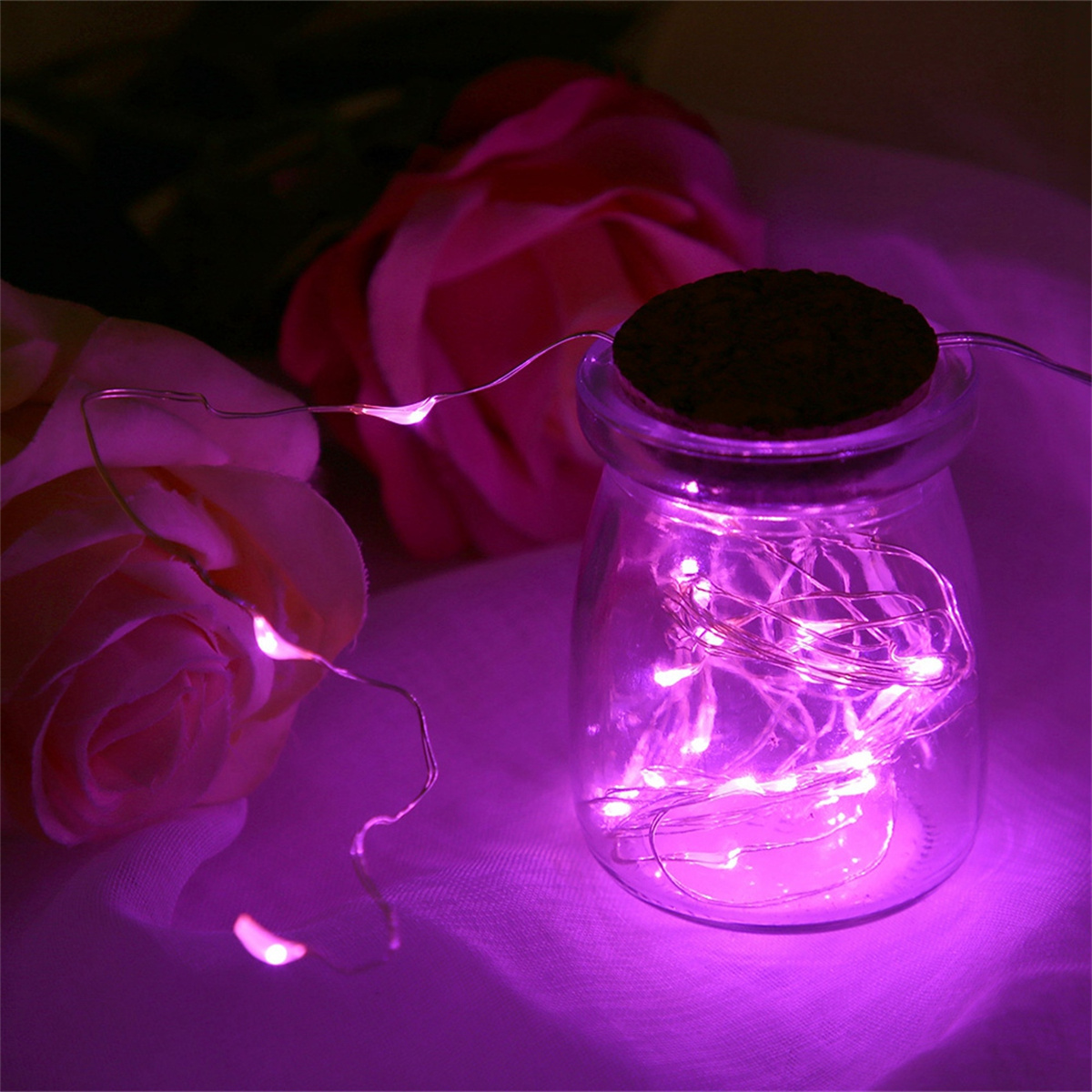 Ein Glas mit Lichterketten und einem Korkdeckel, neben rosa Rosen. Die Szene hat einen violetten Farbton.