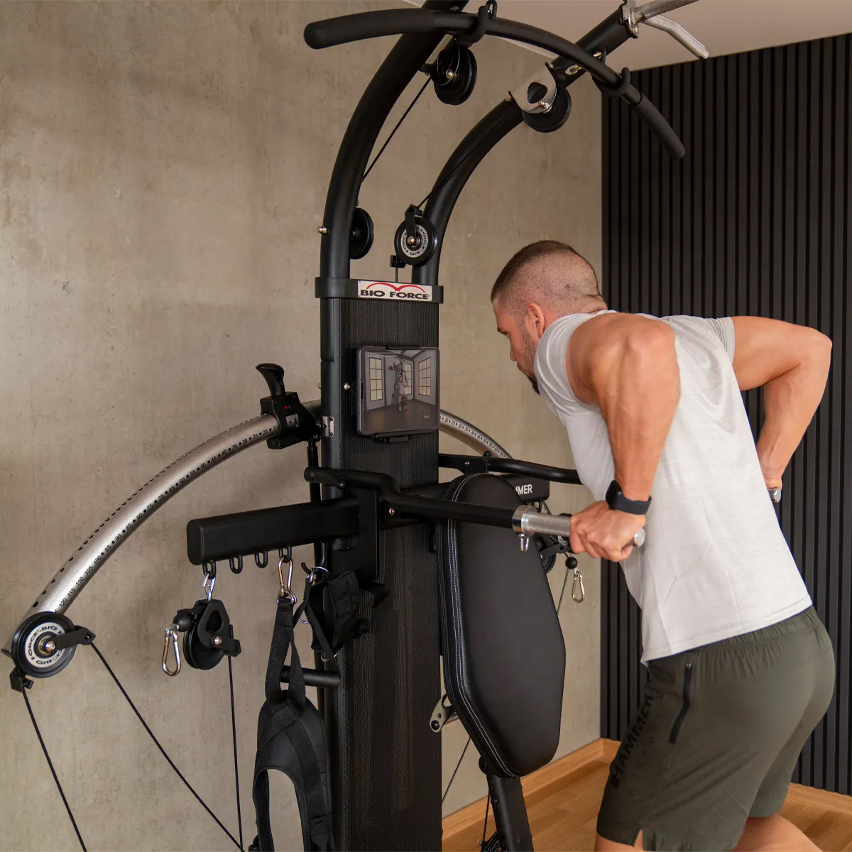 Ein Mann trainiert in einem Heim-Fitnessstudio. Er trägt ein weißes Hemd und Shorts. Das Studio ist schwarz.