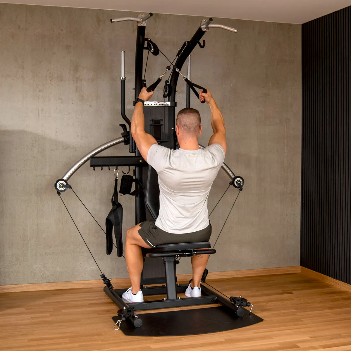 Mann benutzt Fitnessgerät. Graue Wand im Hintergrund.