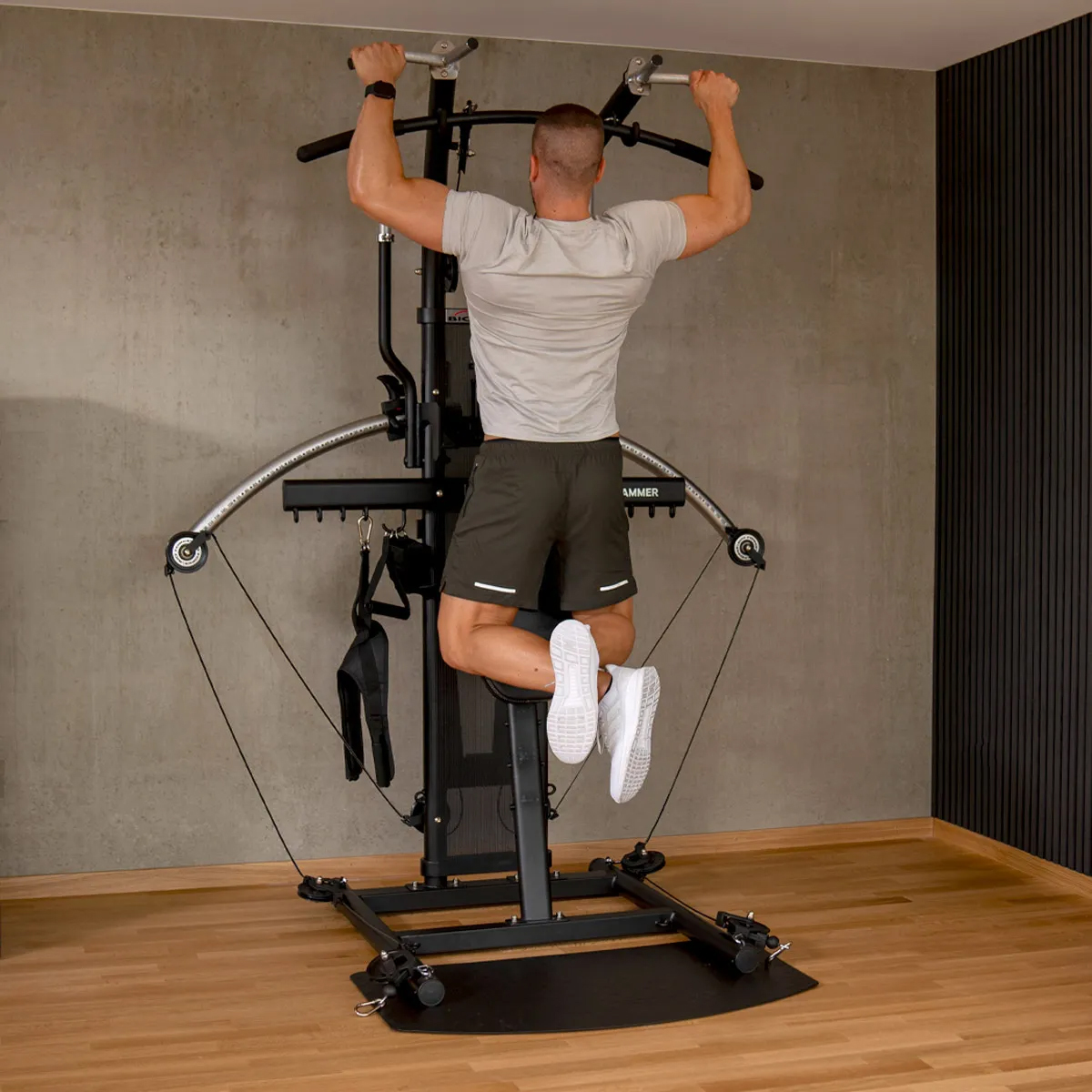 Mann macht Klimmzüge an einer Heimtrainingsmaschine. Er ist ohne Hemd und muskulös.