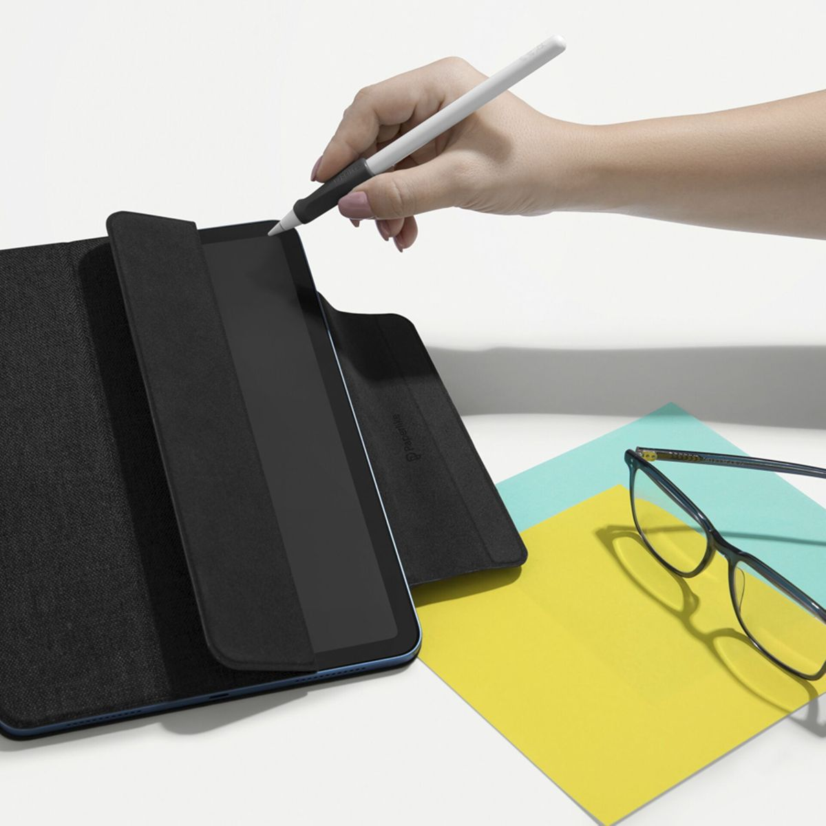 Hand benutzt einen Stift auf einem Tablet. Brille und Papiere liegen daneben.