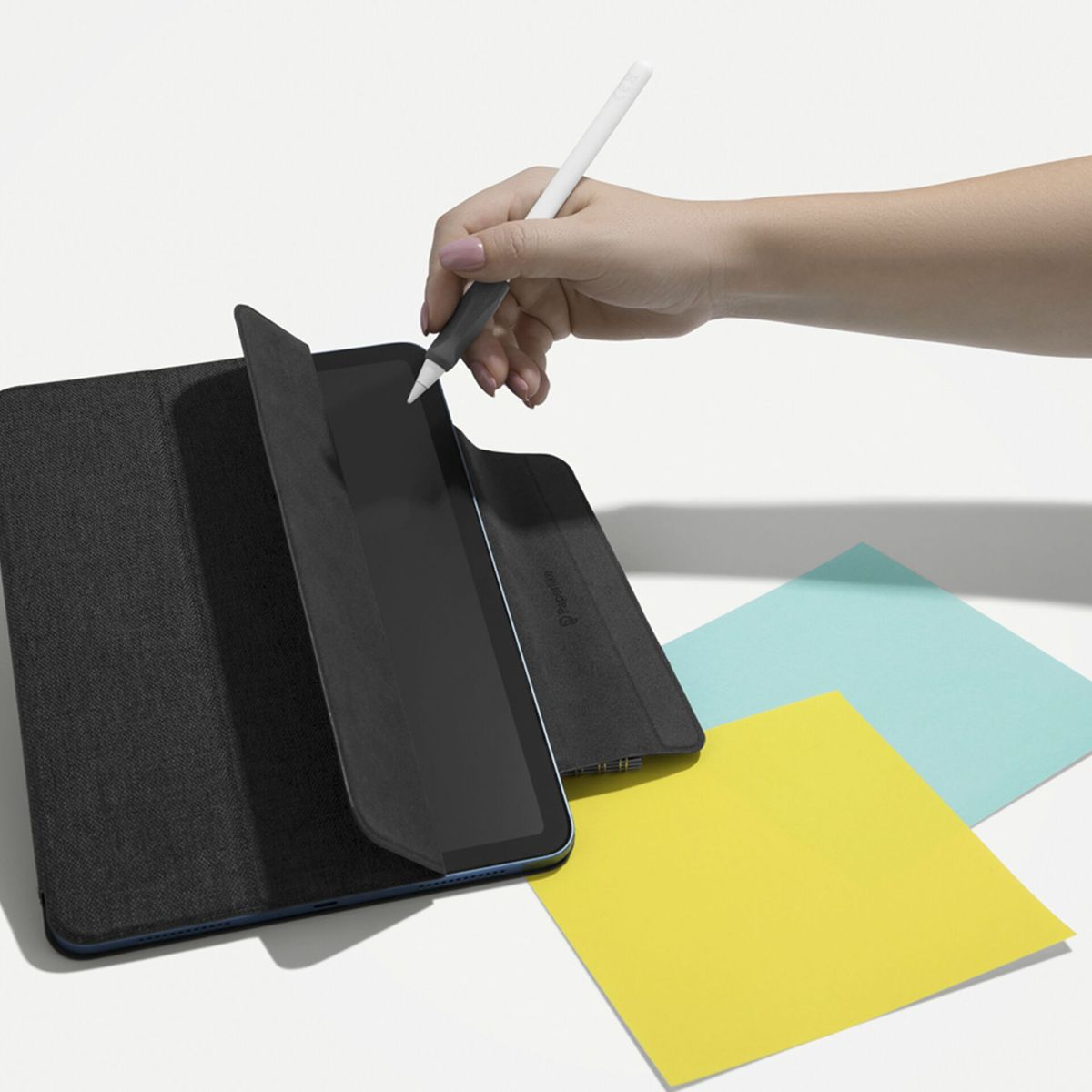 Ein Tablet mit dunkler Hülle, ein Stift in der Hand und bunte Haftnotizen.