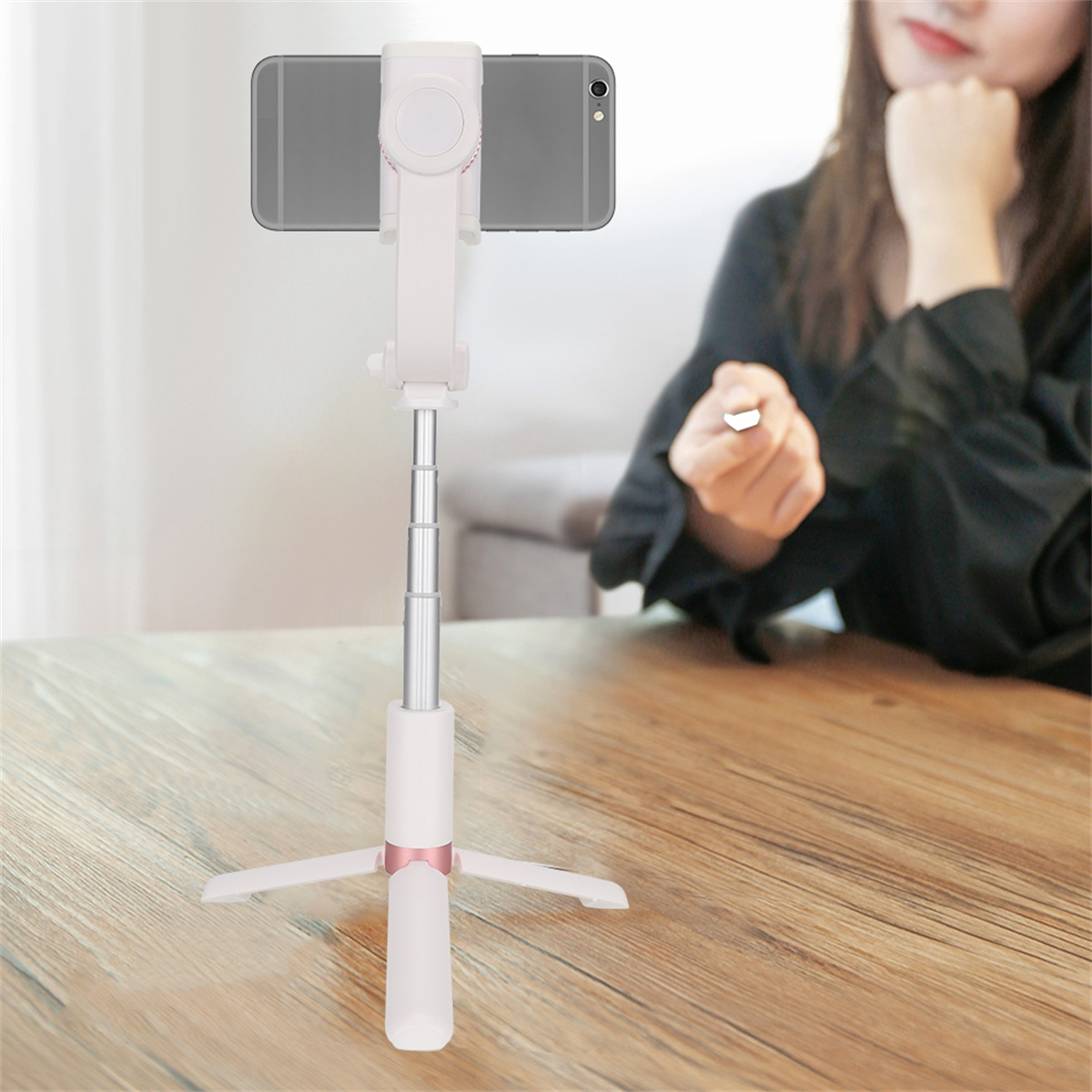 Ein Selfie-Stick mit montiertem Telefon. Eine Frau ist im Hintergrund und schaut es an.