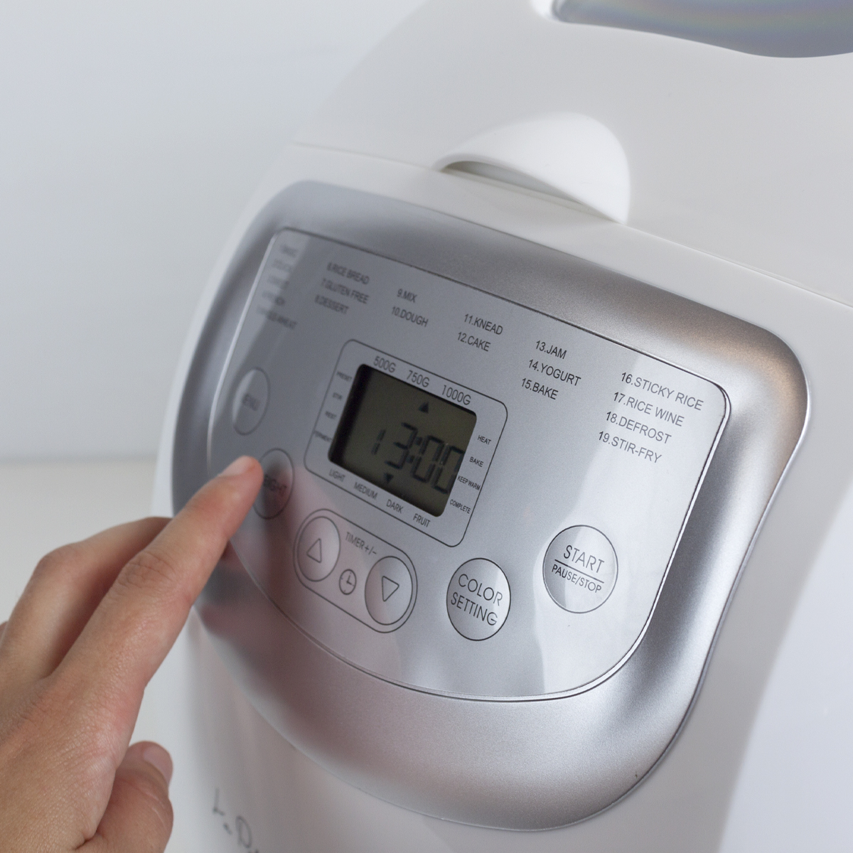 Ręka naciska przycisk na białej maszynie do chleba.