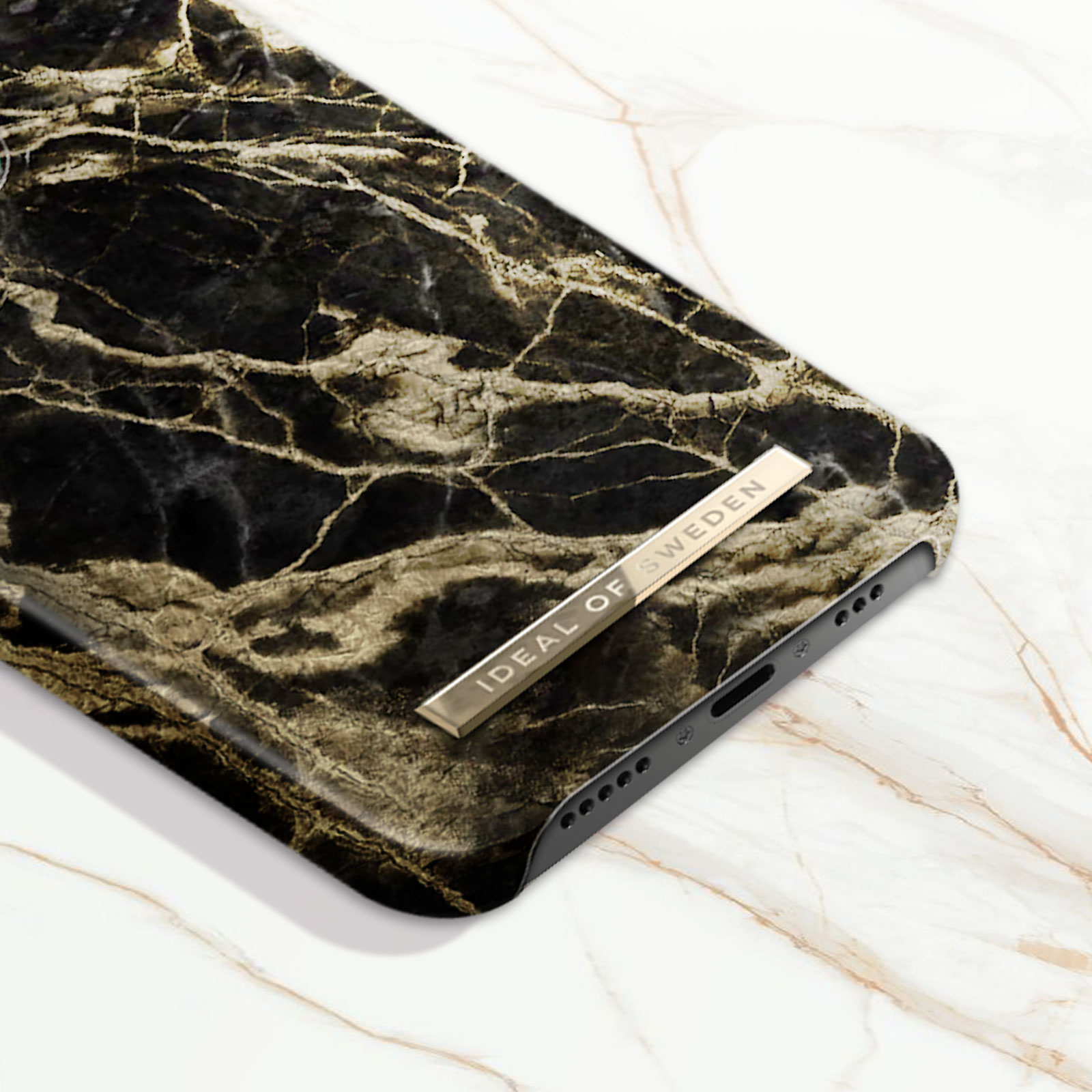 Primo piano di una custodia per telefono in marmo nero e oro con una barra dorata 'IDEAL OF SWEDEN'.