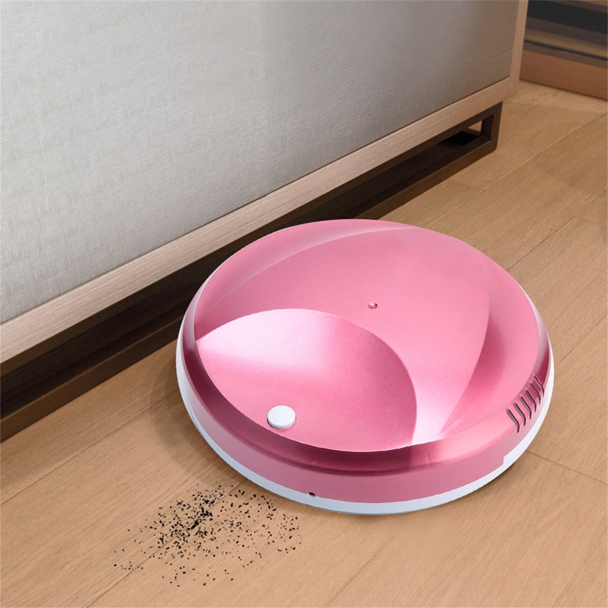 Ein pinkfarbener Roboter-Staubsauger auf einem Holzboden. Er steht neben einem Holzschrank. Ein kleiner Schmutzhaufen.