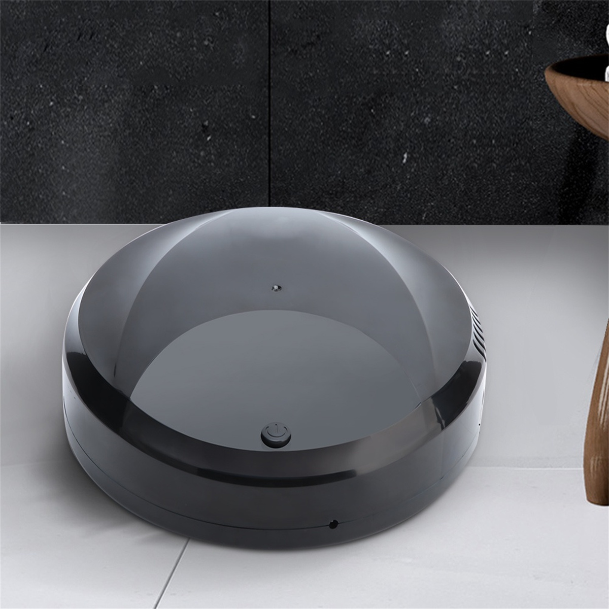 Ein schwarzer, runder Roboter-Staubsauger auf einem weiß gefliesten Boden mit einem Ein-/Aus-Schalter.