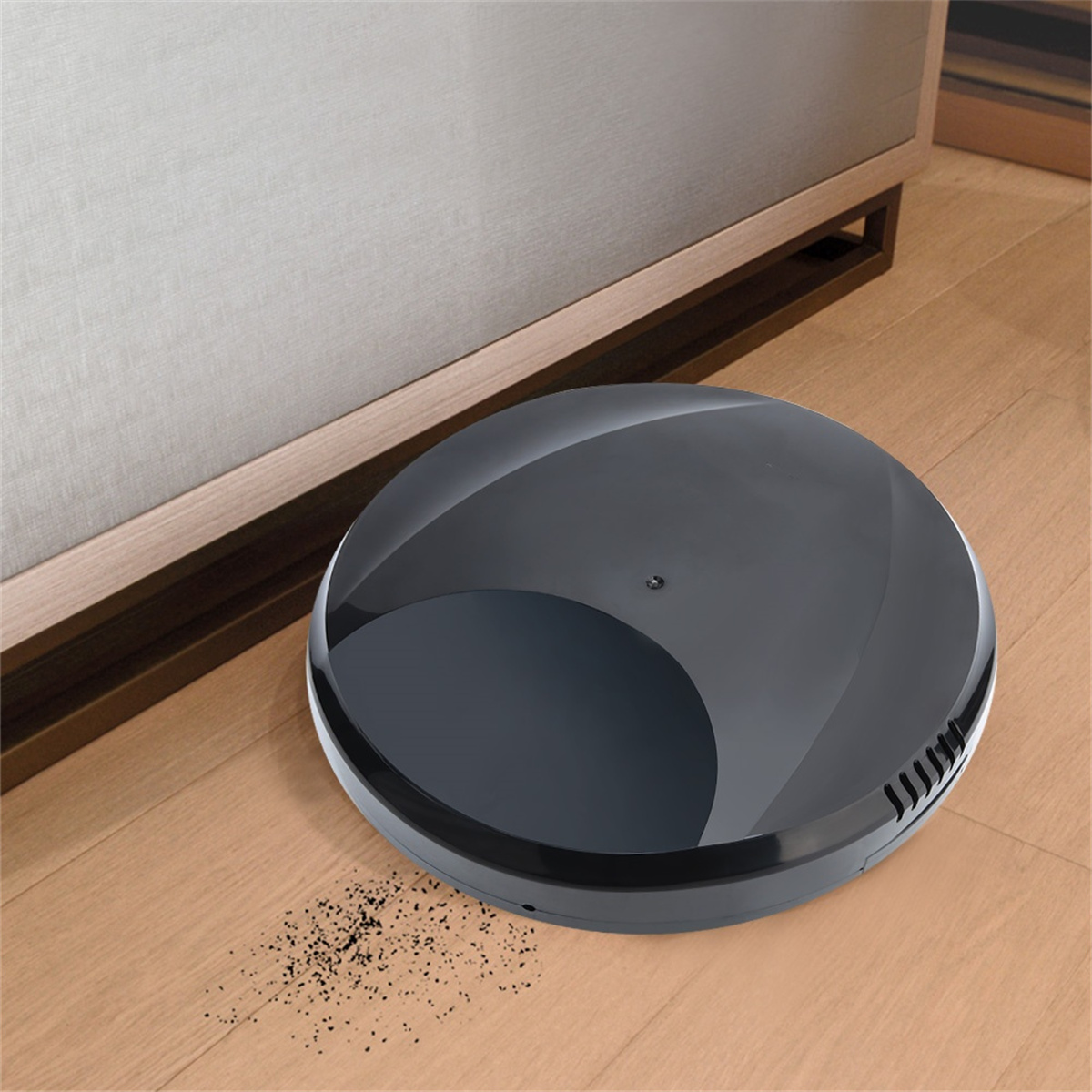 Schwarzer Roboter-Staubsauger auf Holzboden in der Nähe eines Bettes.
