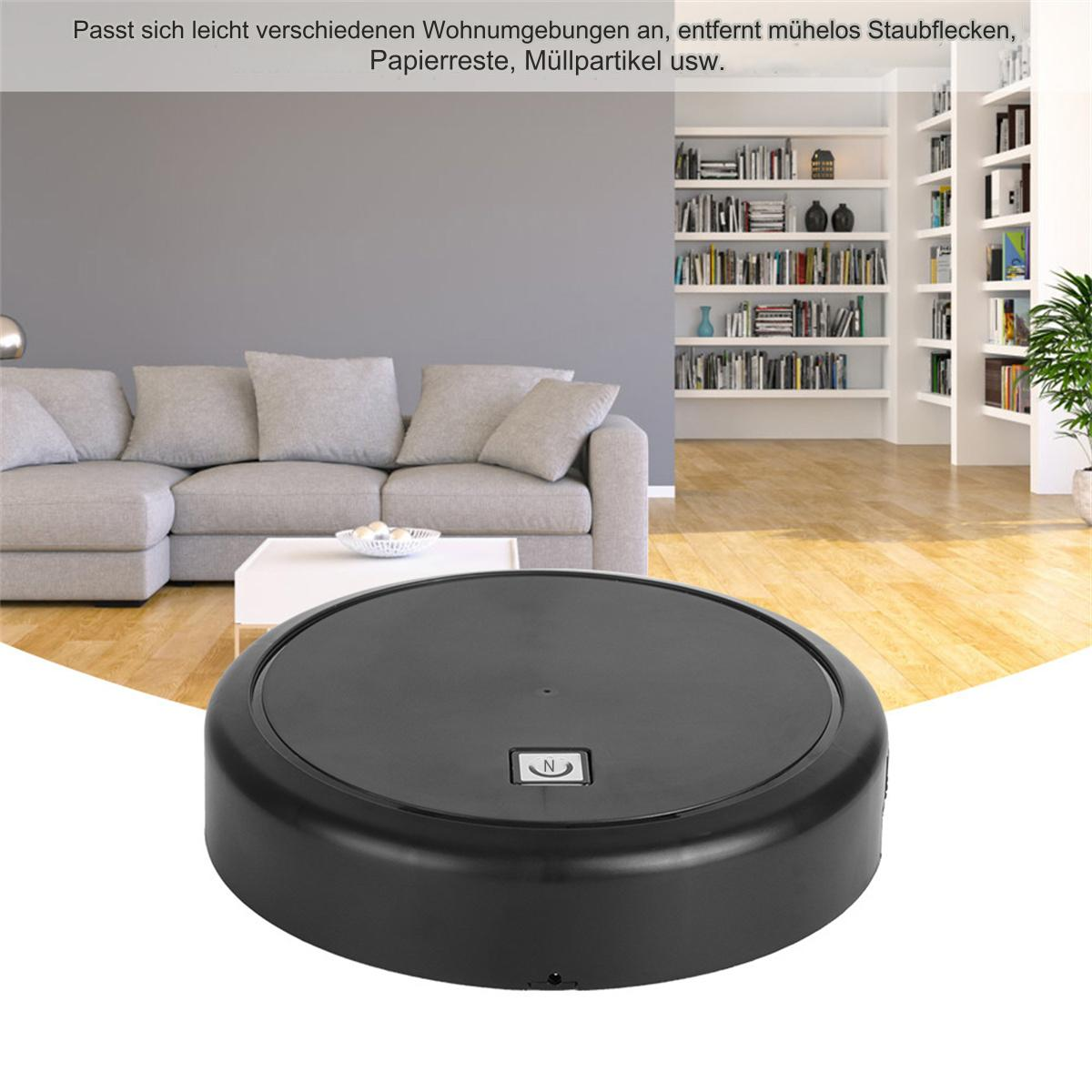 Ein schwarzer Roboter-Staubsauger auf dem Boden. Im Hintergrund ein weißer Tisch, Sofa und Bücherregale.