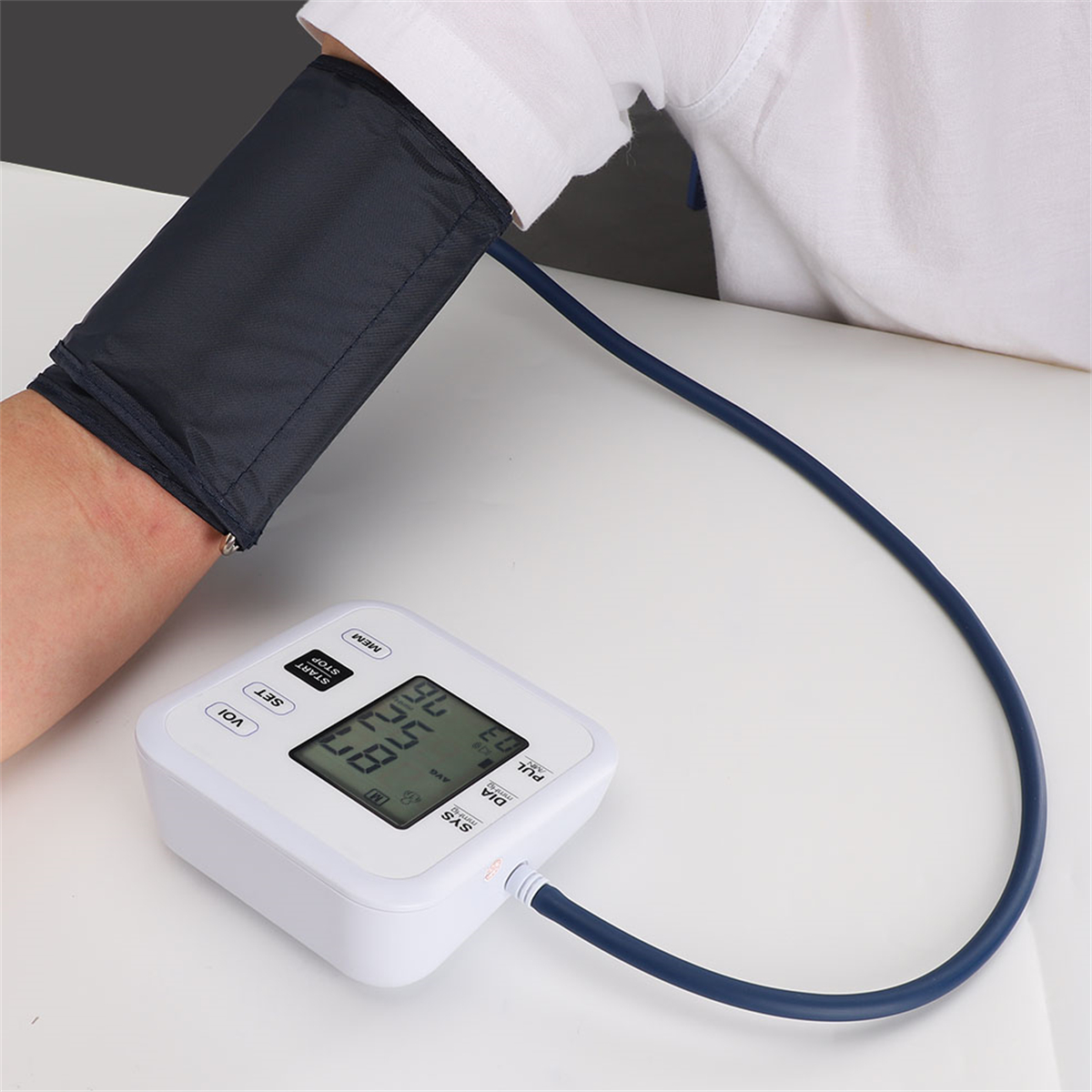 Person mit Blutdruckmanschette am Arm, verbunden mit einem weißen Blutdruckmessgerät.
