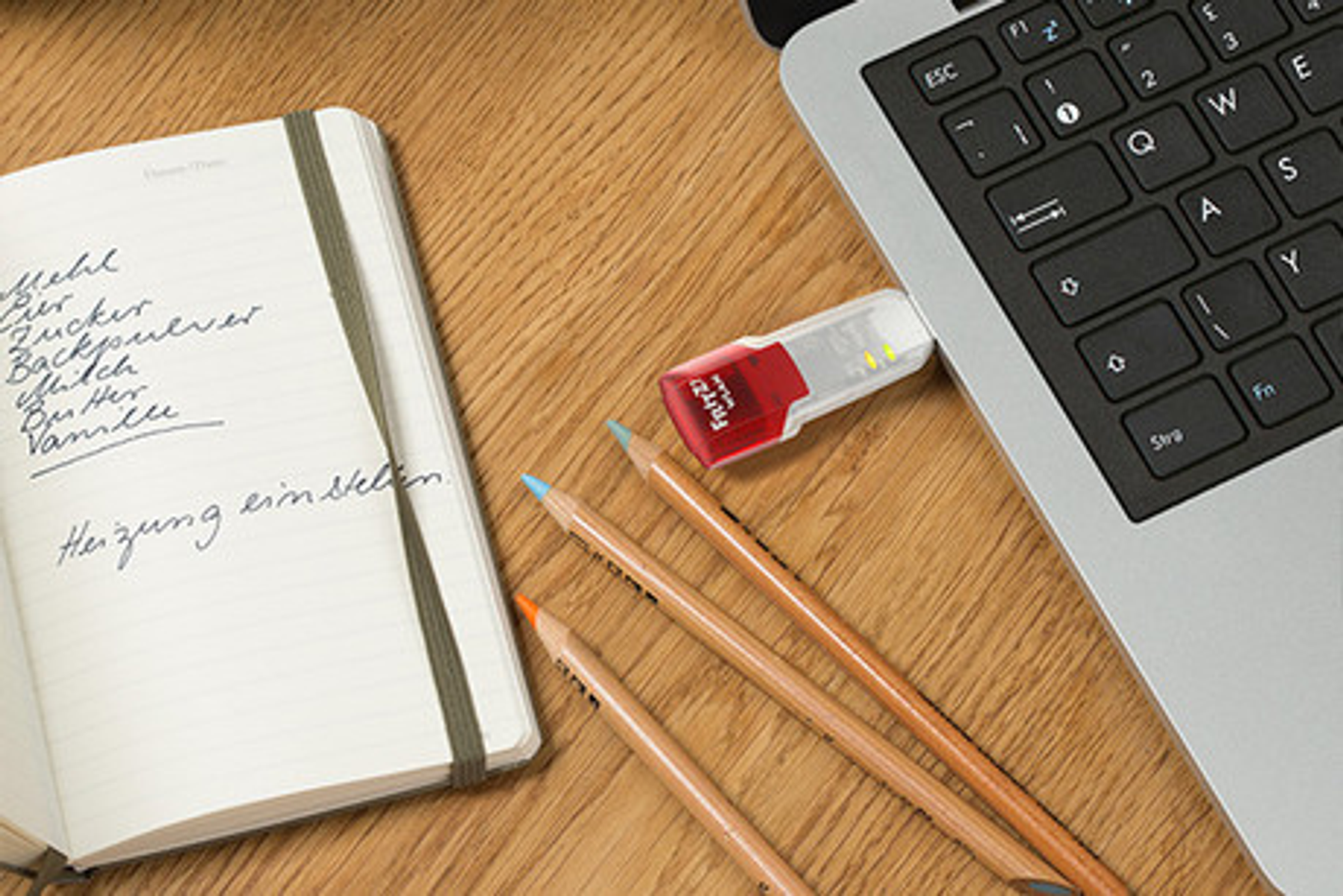 Quaderno con scrittura a mano e matite accanto a un laptop con una chiavetta USB inserita.