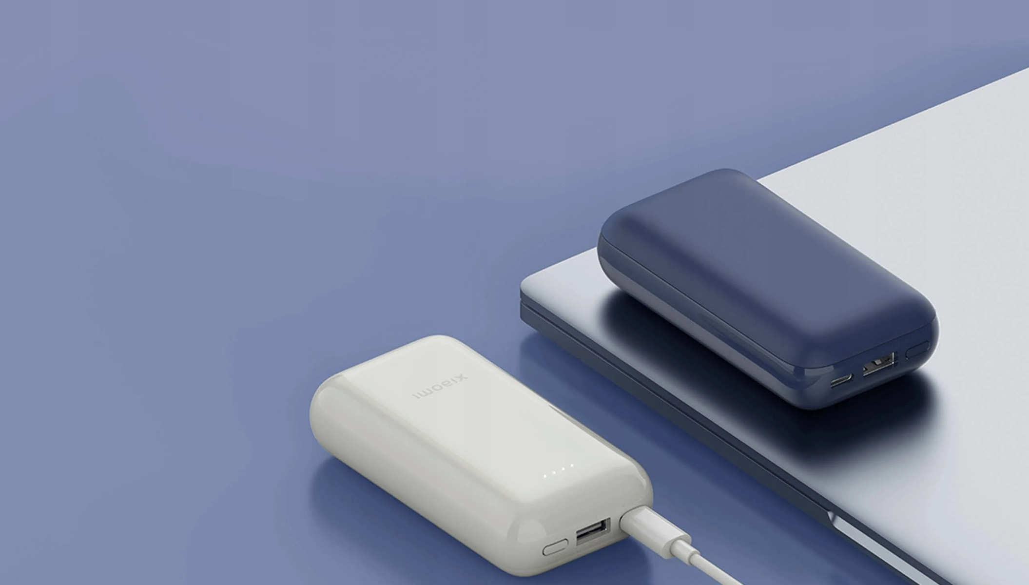 Twee draagbare powerbanks: één wit, één marineblauw, op een blauw oppervlak.