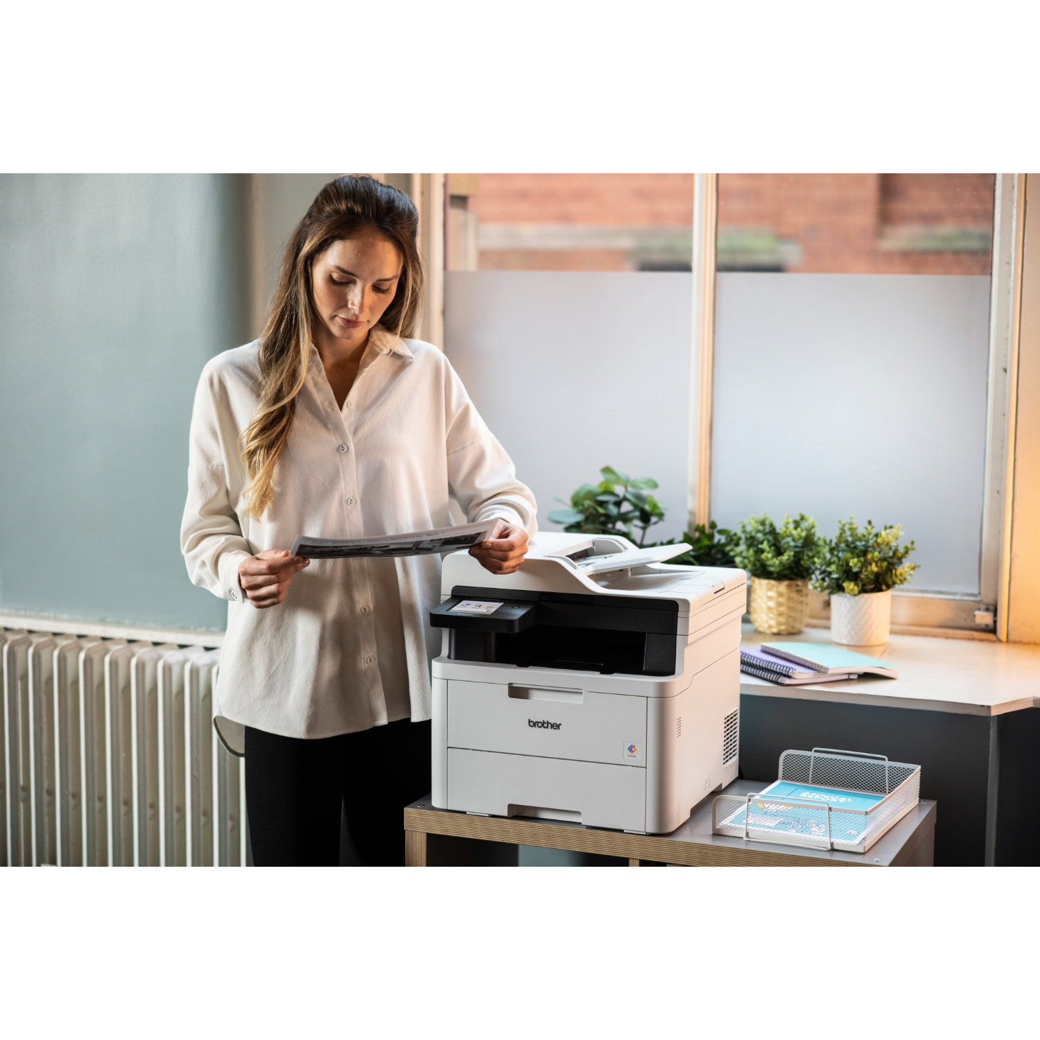 Kobieta w białej koszuli przegląda wydruk z białej drukarki na drewnianym biurku.