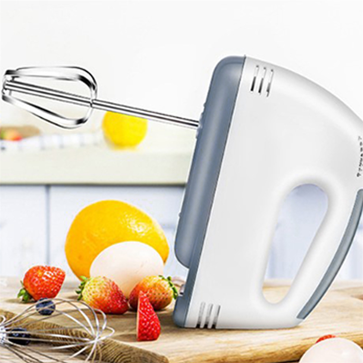 Weißer und grauer Handmixer mit silbernem Schneebesen und Zutaten wie Eiern und Erdbeeren.