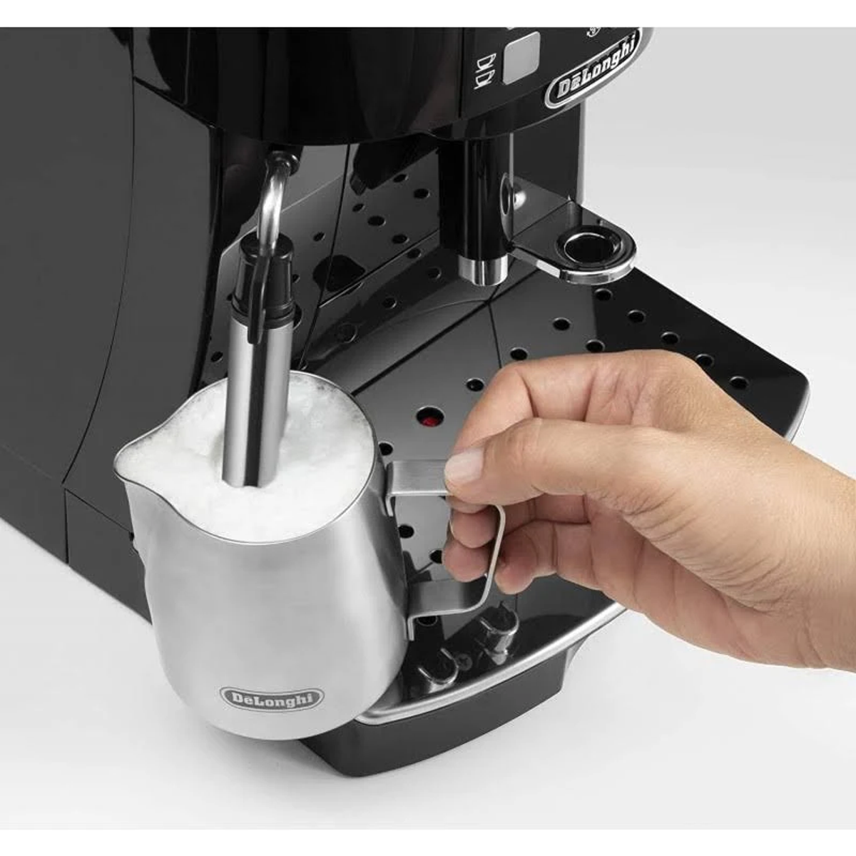 Ręka wlewa mleko do dzbanka ze stali nierdzewnej do spieniania mleka, podłączonego do ekspresu do kawy Delonghi.