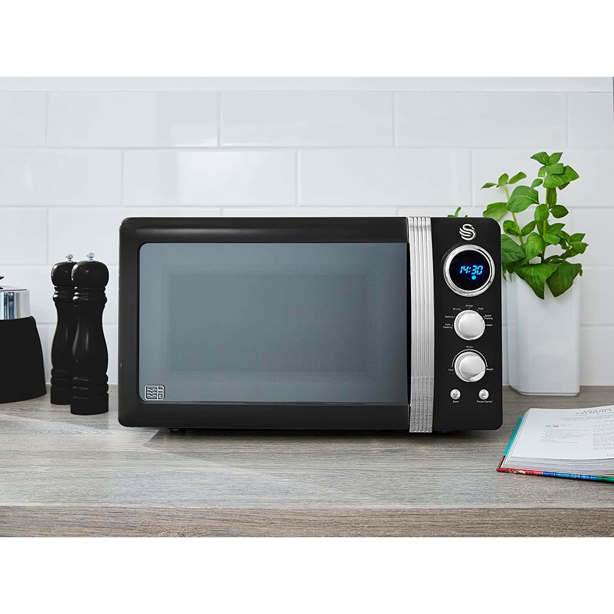 Un horno microondas retro negro con reloj digital sobre una pared de azulejos blancos.