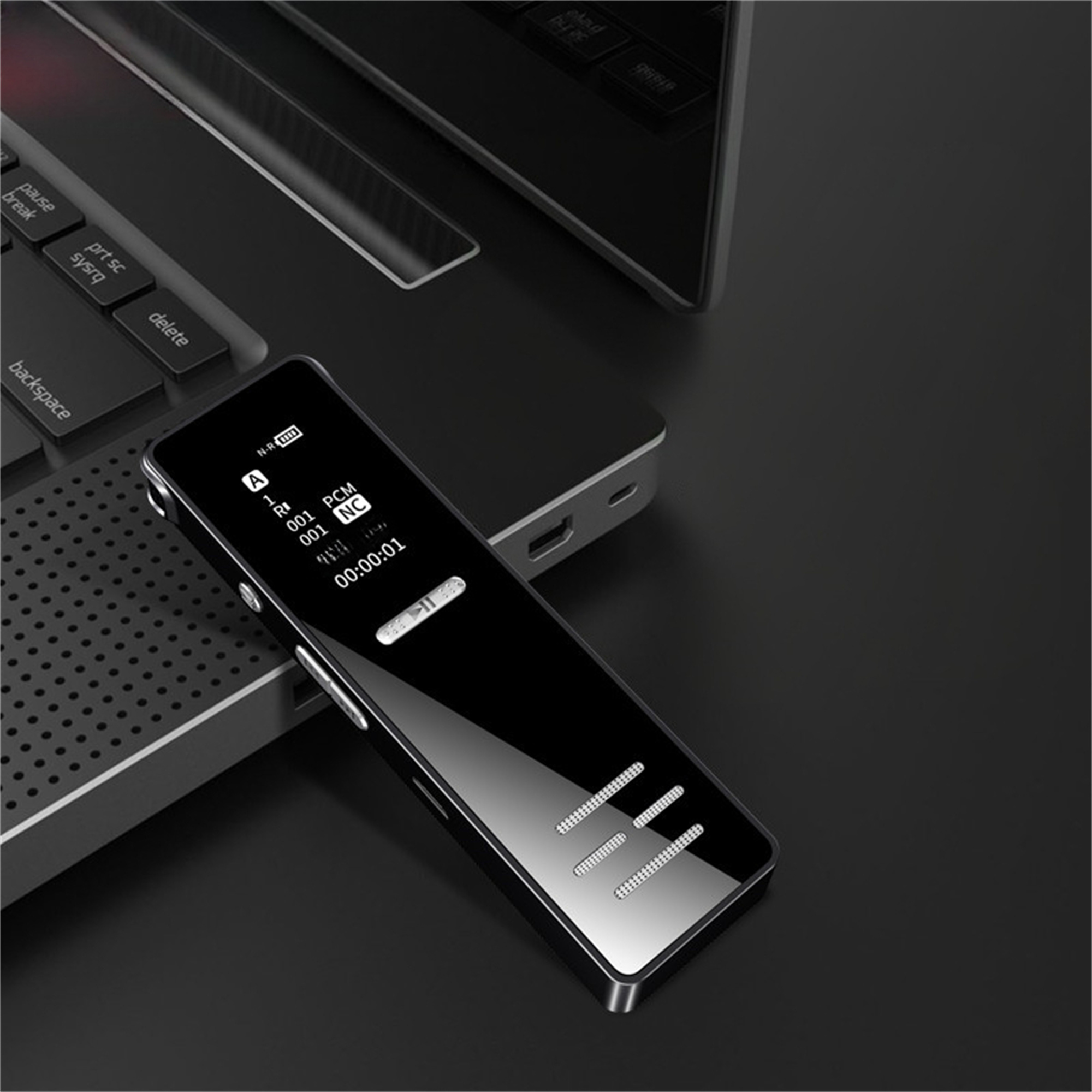 Schwarzes digitales Sprachaufnahmegerät mit Display auf dunkler Oberfläche, in der Nähe eines Laptops.