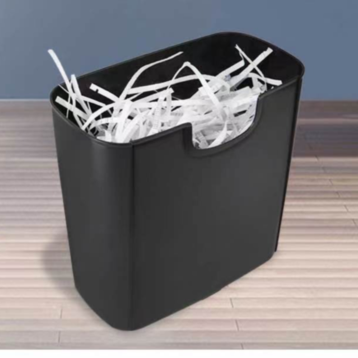 Schwarze, rechteckige Tonne mit zerkleinertem weißem Papier auf einem Holzboden.