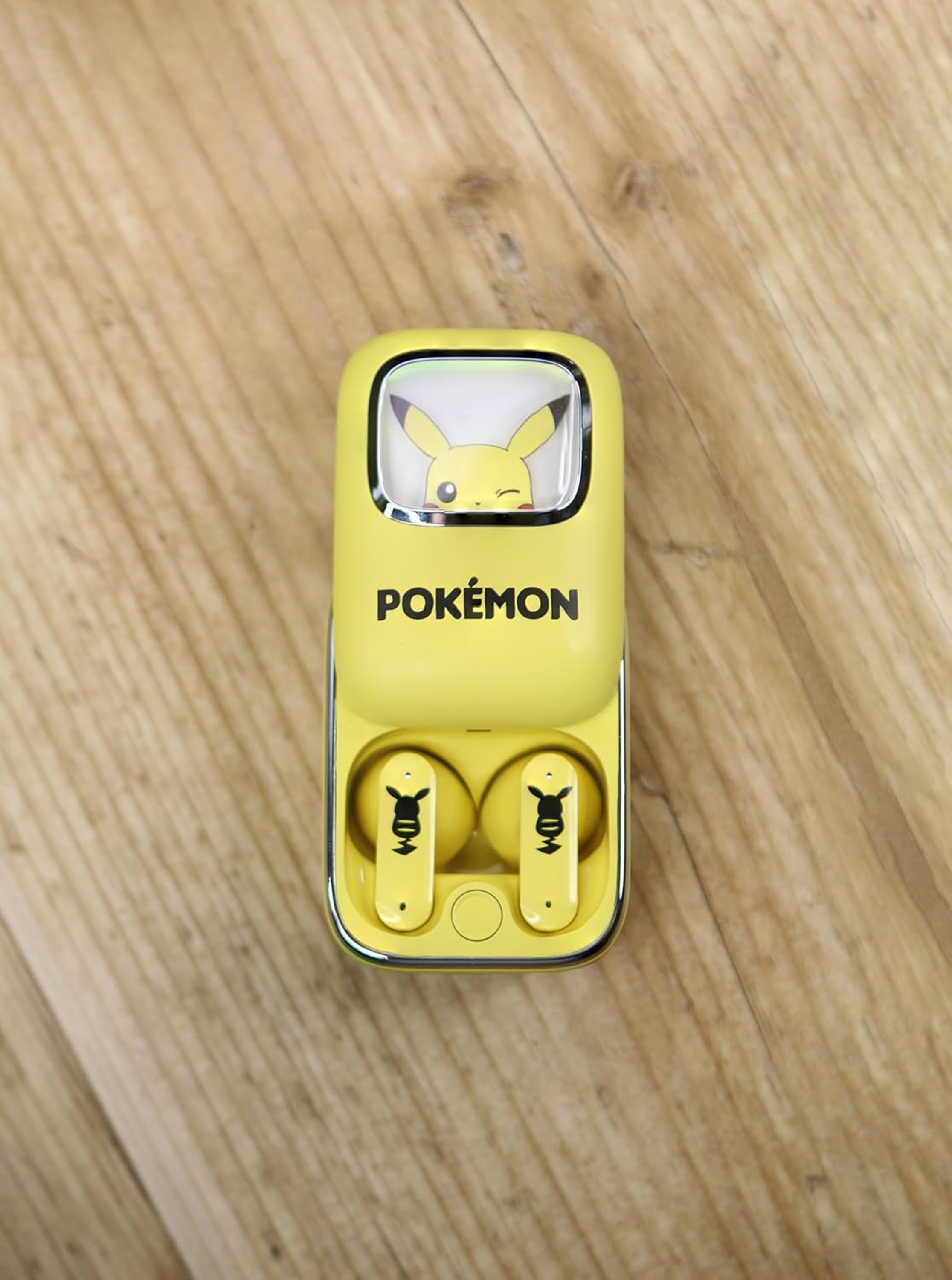 Żółte słuchawki Pokemon w etui ładującym na drewnianej powierzchni.