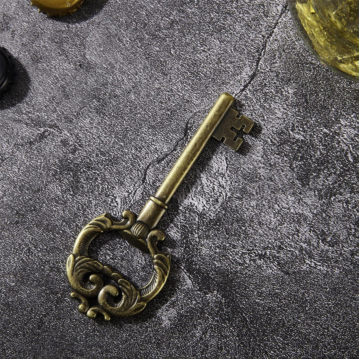 Goldener Flaschenöffner in Schlüsselform auf strukturierter grauer Oberfläche. Der Schlüssel hat einen dekorativen Griff.