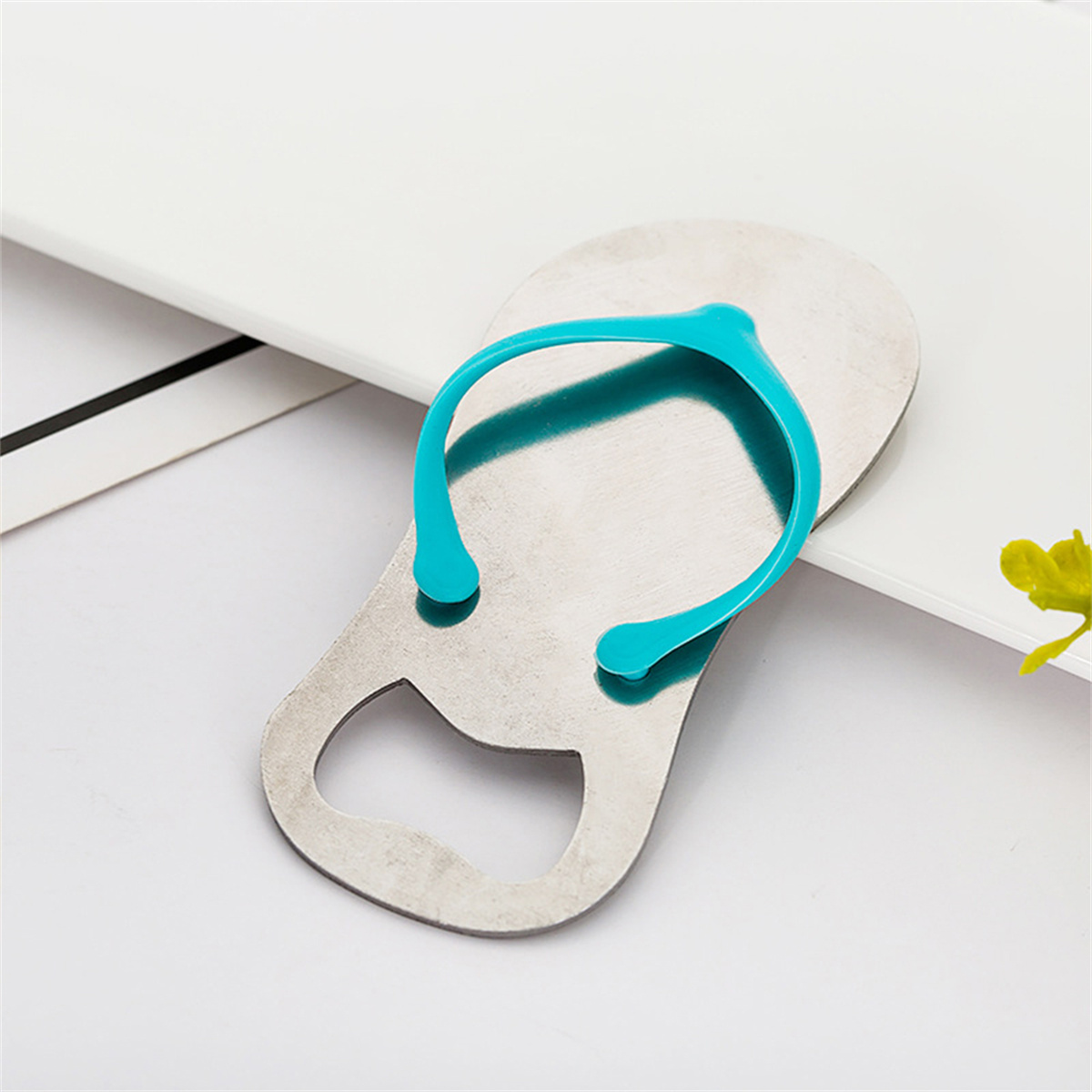 Ein metallener Flaschenöffner in Flip-Flop-Form mit blauem Riemen, auf weißer Oberfläche.