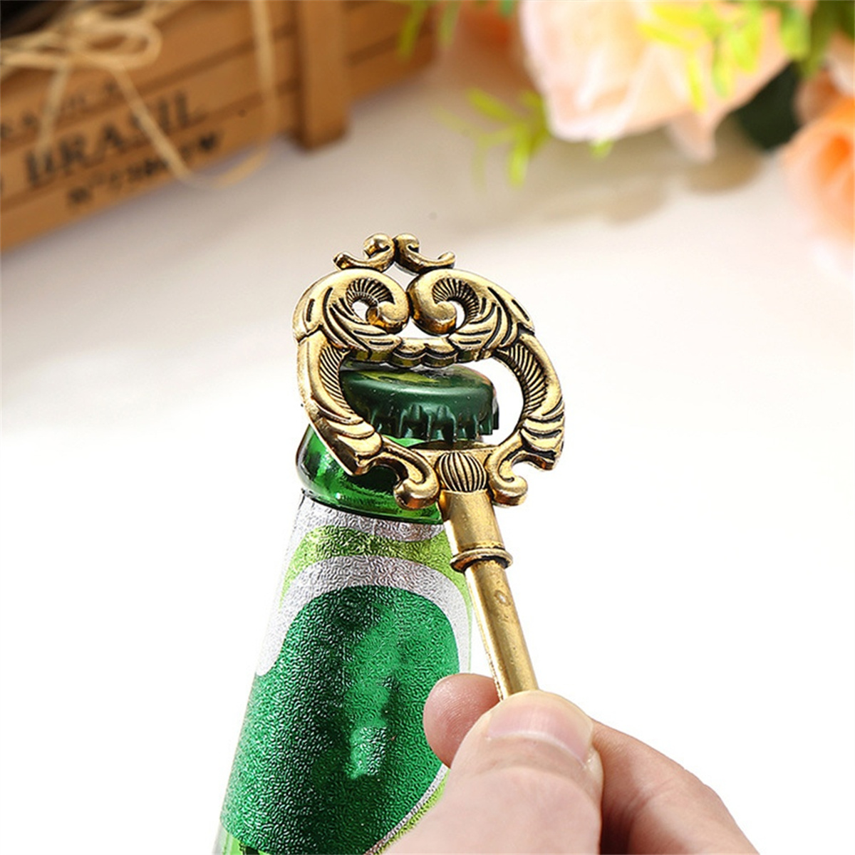 Eine Hand öffnet eine Flasche mit einem goldfarbenen, schlüsselförmigen Flaschenöffner. Grüne Flasche im Hintergrund.