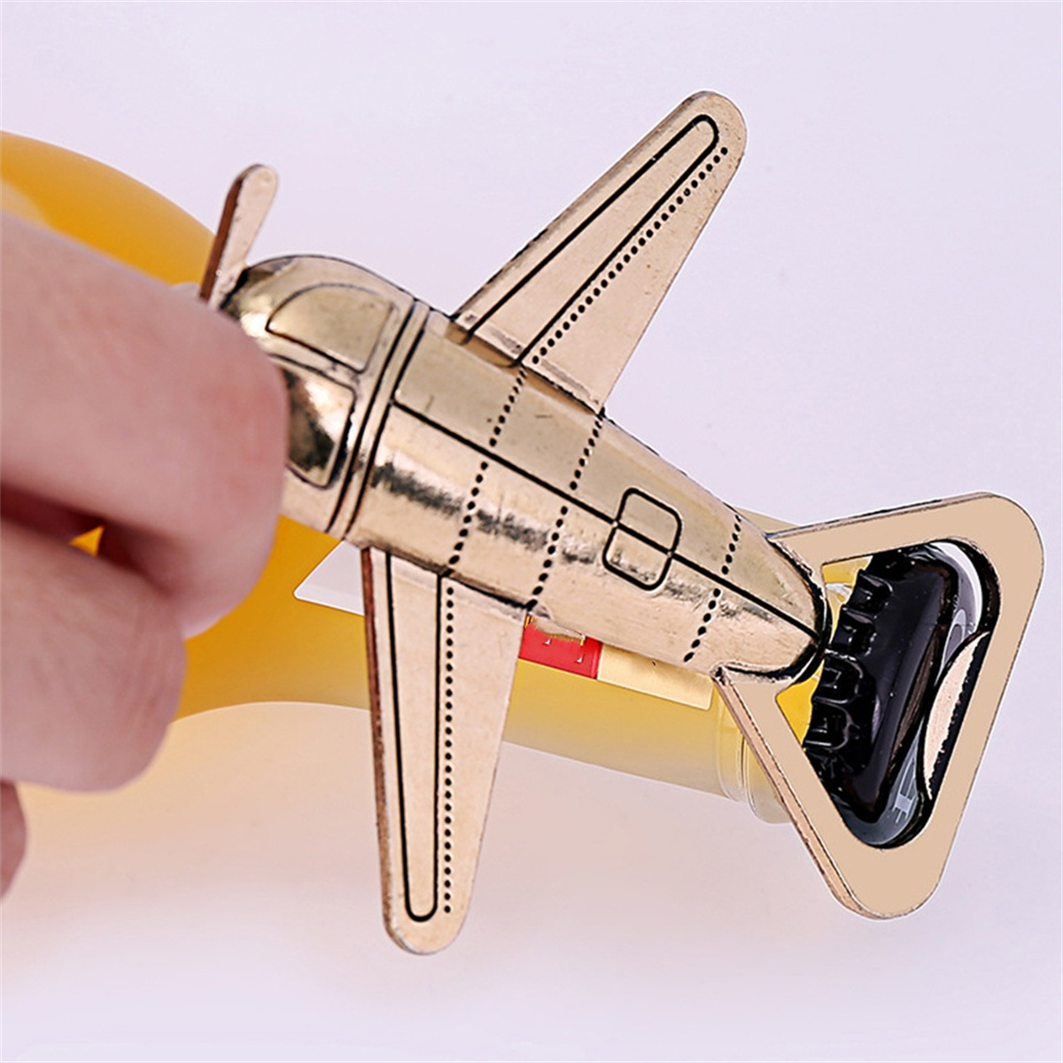 Ein goldfarbener, flugzeugförmiger Flaschenöffner, der eine gelbe Flasche öffnet. Der Flaschenöffner hat ein schwarzes Design.